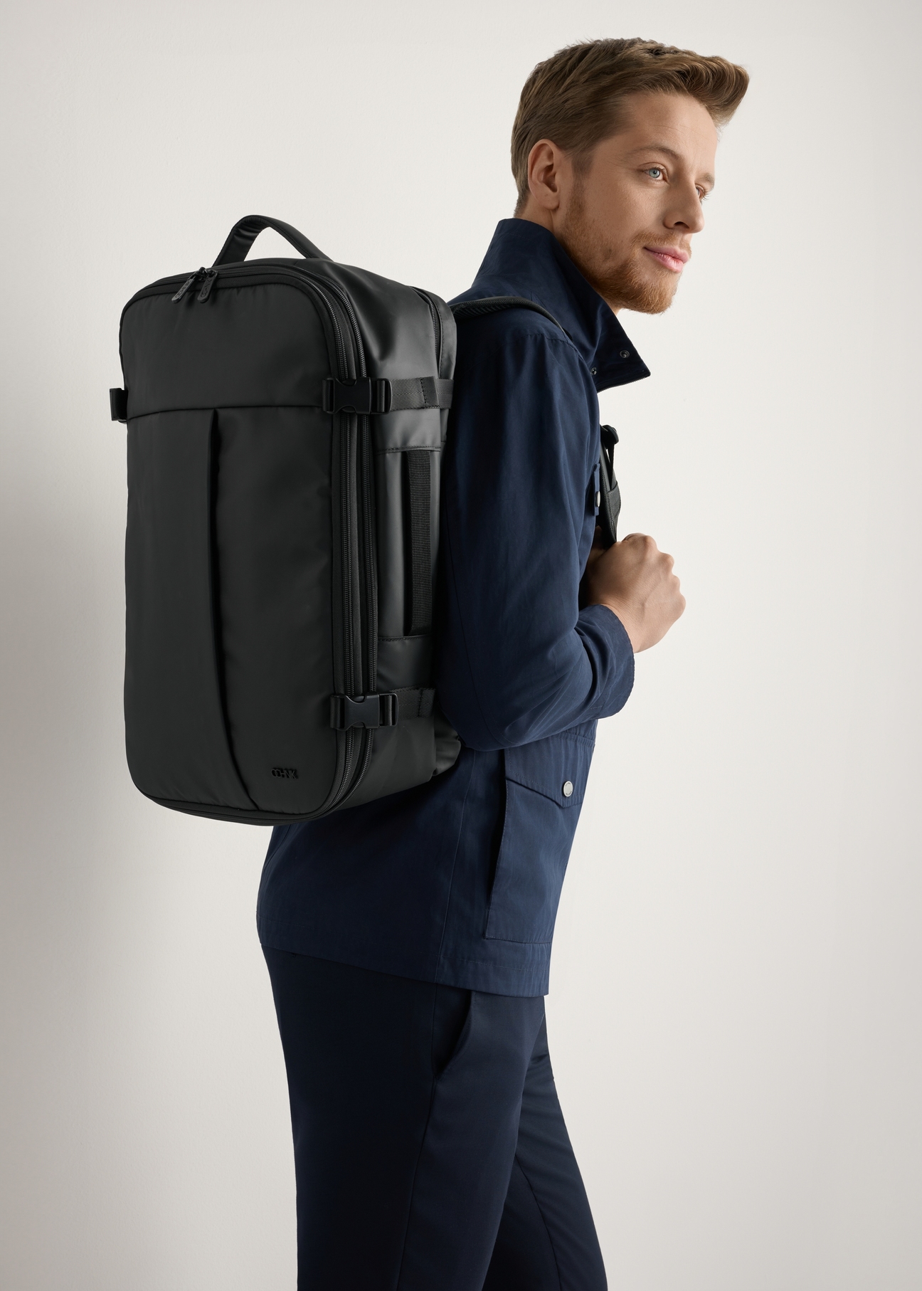 Czarny duży plecak podróżny TORMN-0409-99(W26) - widok produktu lekko po skosie, na modelu, na jasnym tle. Widoczna sylwetka do kolan. 