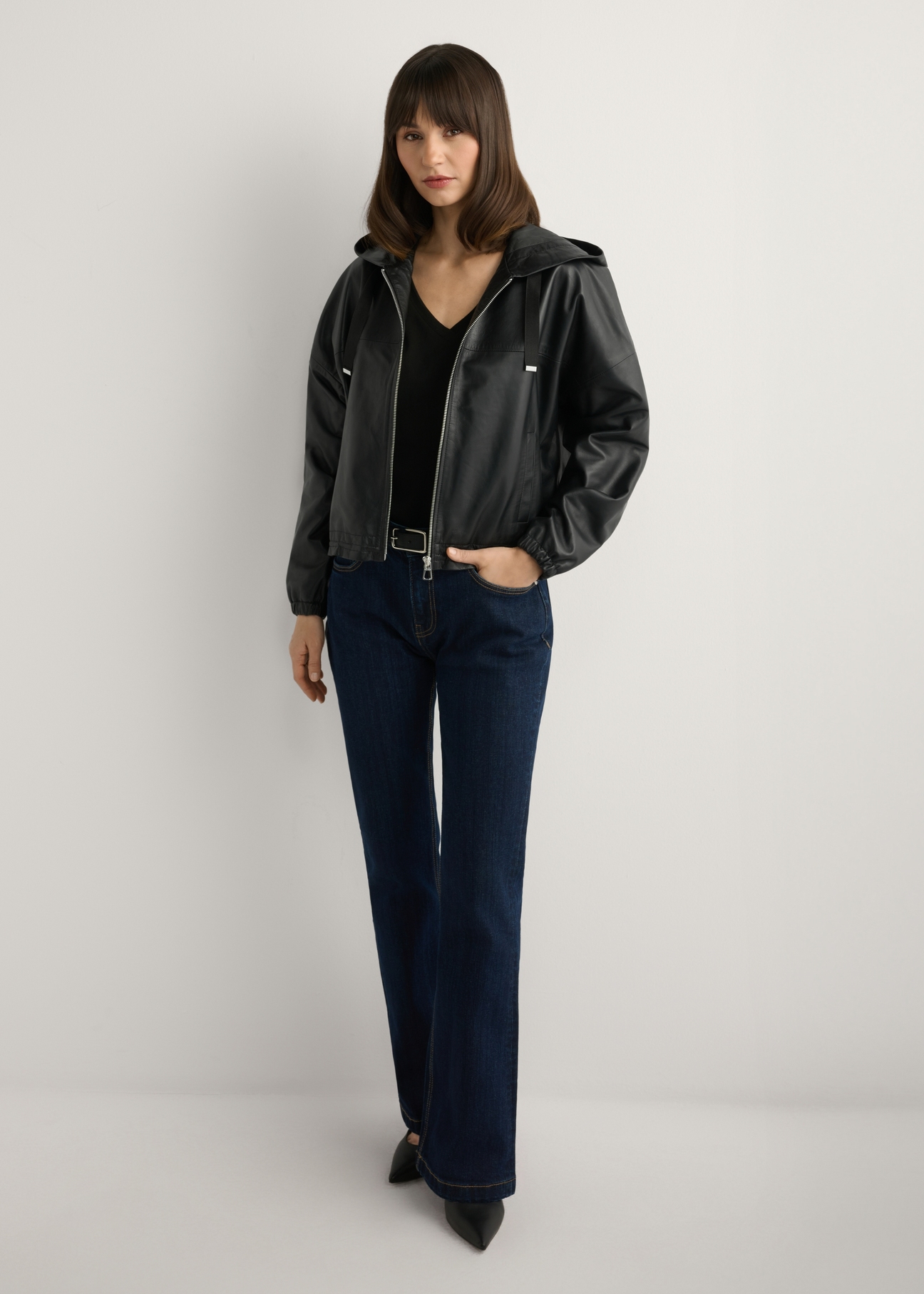 Czarna skórzana kurtka damska z kapturem KURDS-0412-99(W26), widok produktu z przodu na modelce. Widoczna cała sylwetka.