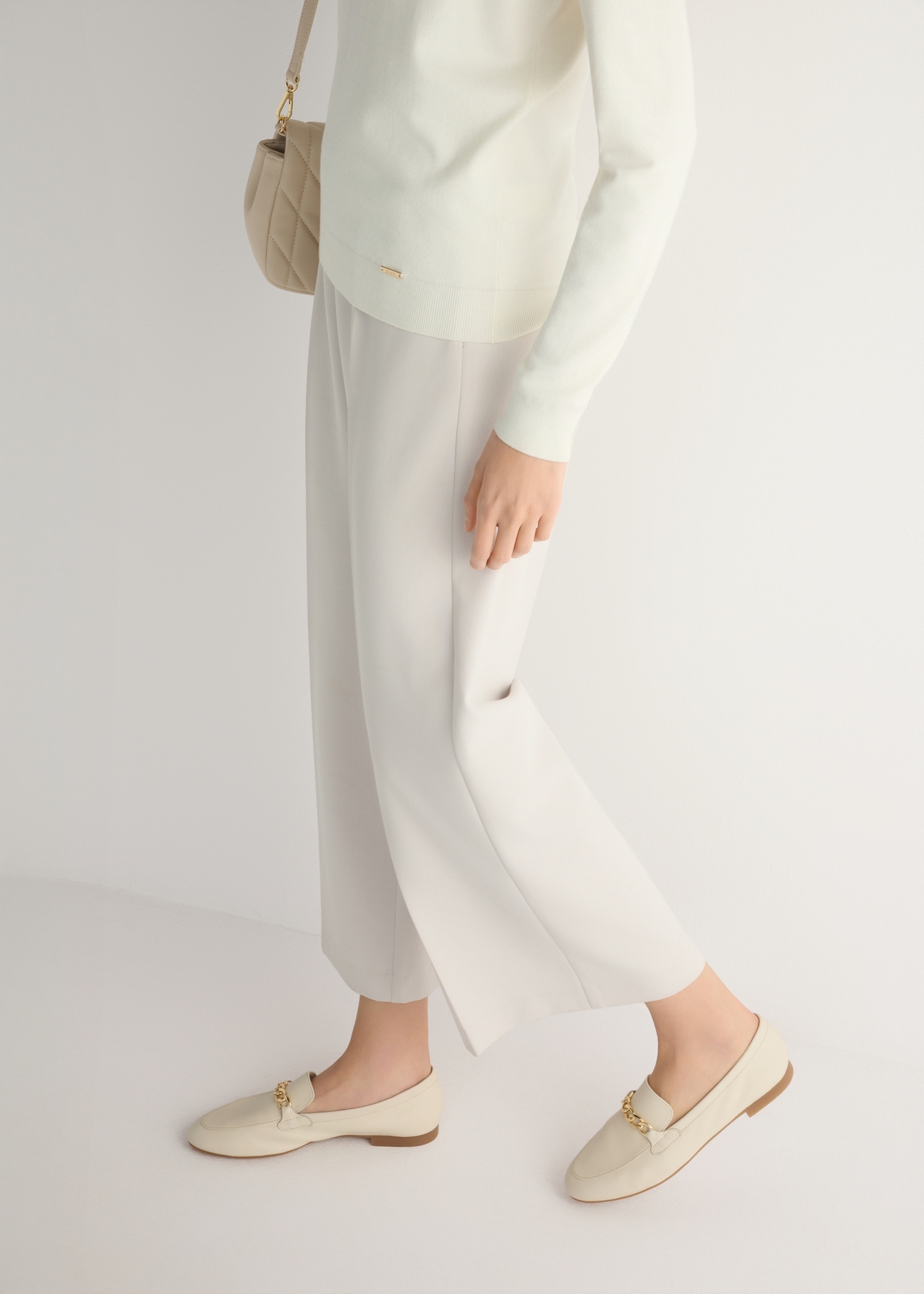 Skórzane kremowe mokasyny damskie z łańcuszkiem BUTYD-0914A-0B(W26), widok produktu od boku na modelce, widoczna połowa sylwetki.