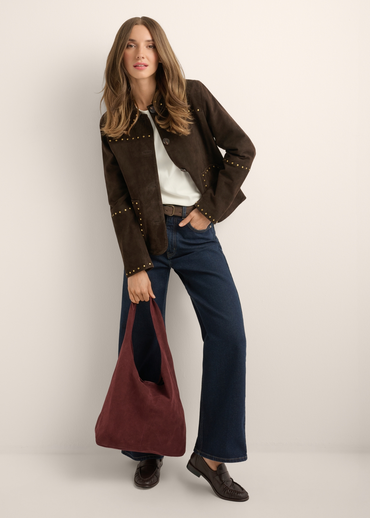 Bordowa zamszowa torebka shopper TORES-1403-4D(Z26) - widok produktu trzymanego przez modelkę w ręku, na jasnym tle. Widoczna cała sylwetka.