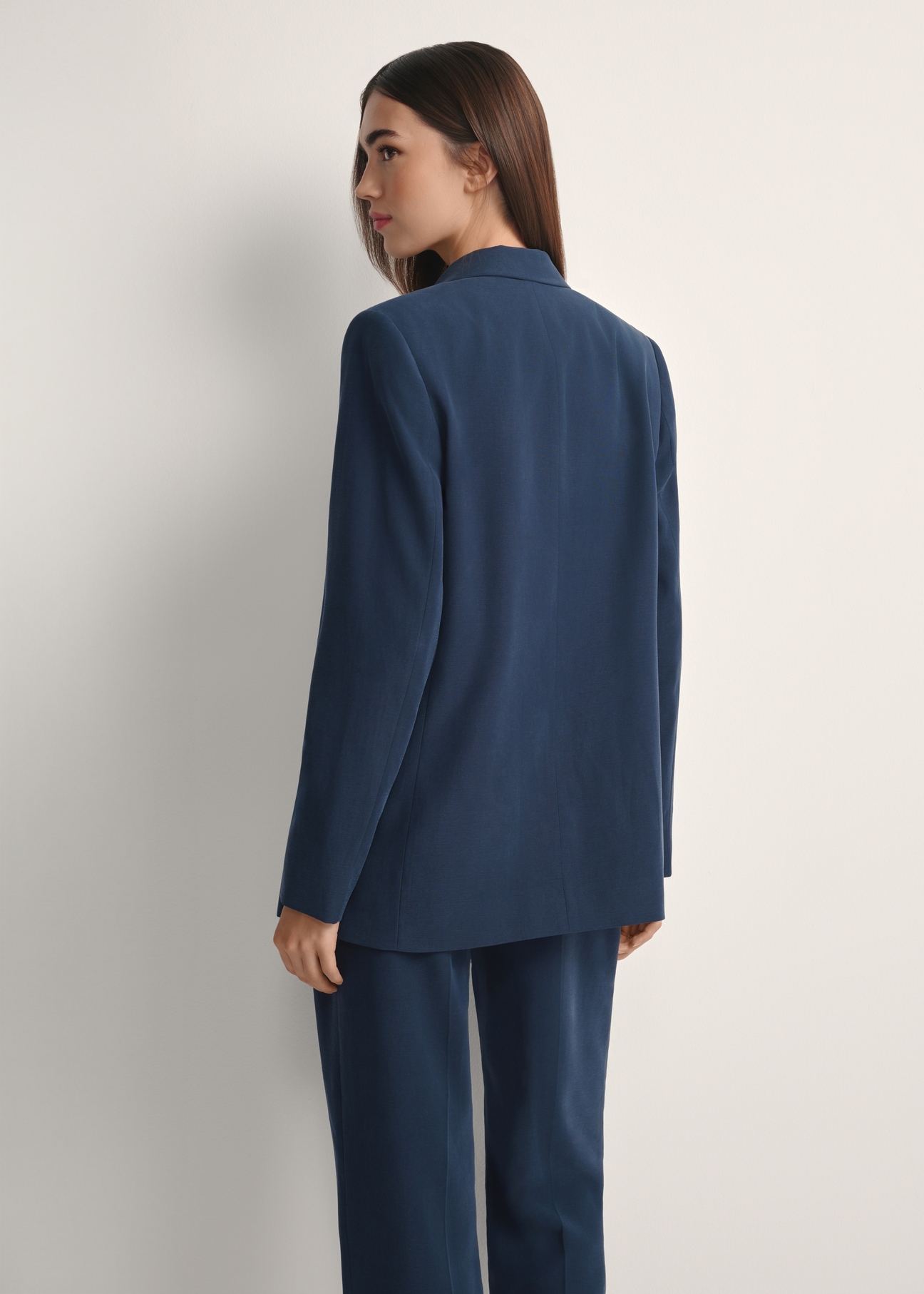 Marynarka damska w kolorze granatowym ZAKDT-0031A-7E(W26), widok produktu z tyłu na modelce. Widoczna połowa sylwetki.