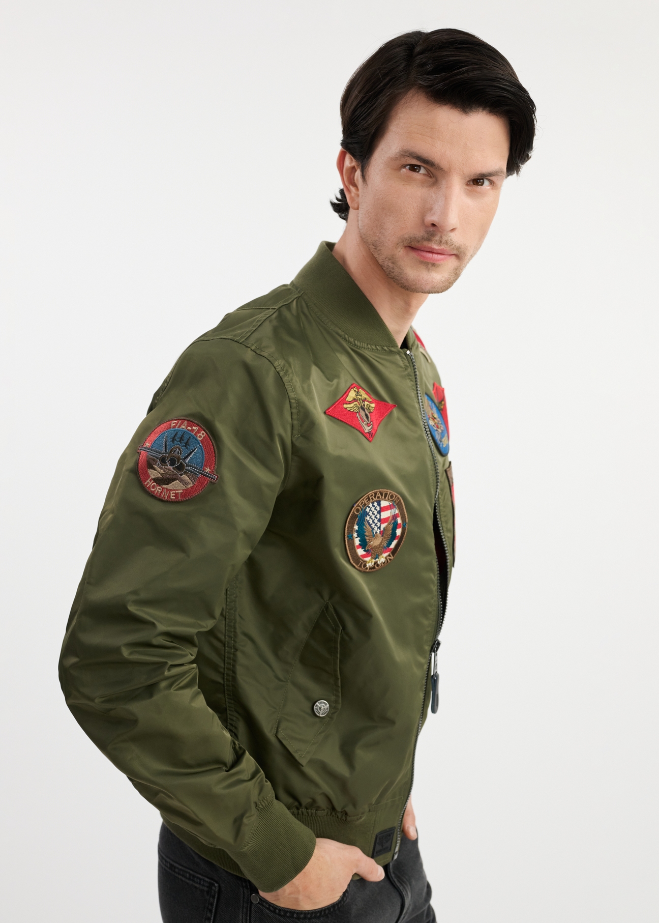 Oliwkowa męska kurtka pilotka TOP GUN KURMT-0381-57(W25) - widok z boku na modelu na białym tle. Widoczna połowa sylwetki. 