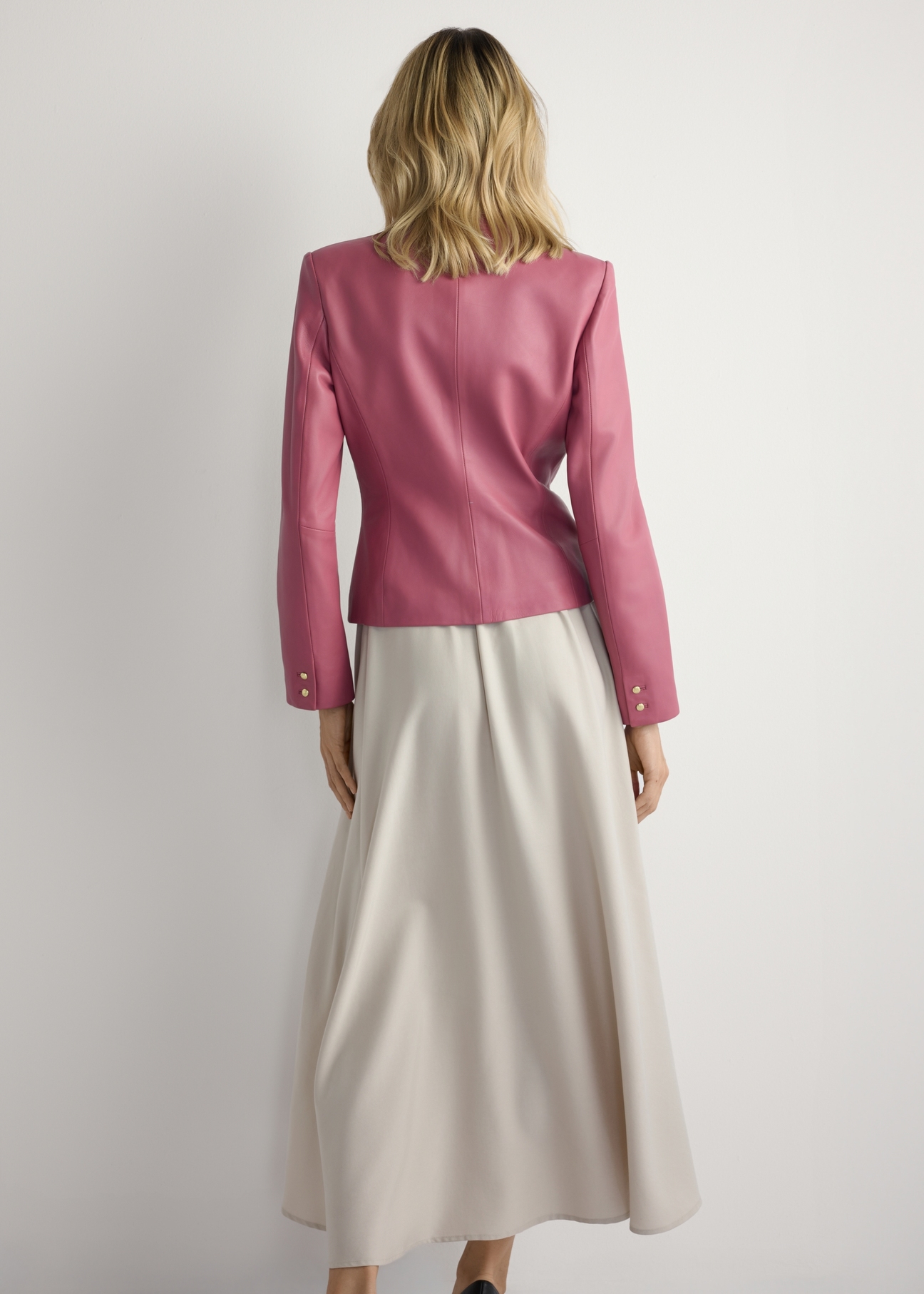 Różowa skórzana marynarka damska KURDS-0599-5D(W26) - widok produktu z tyłu, na modelce, na jasnym tle. Widoczna cała sylwetka. 