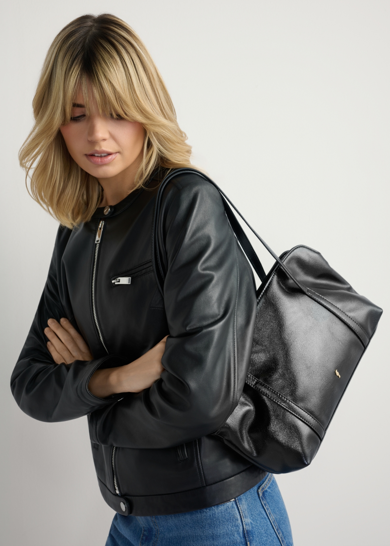 Czarna torebka damska z połyskiem TOREC-1205-9F(W26) - widok produktu lekko po skosie, na modelce, na jasnym tle. Widoczna połowa sylwetki. 