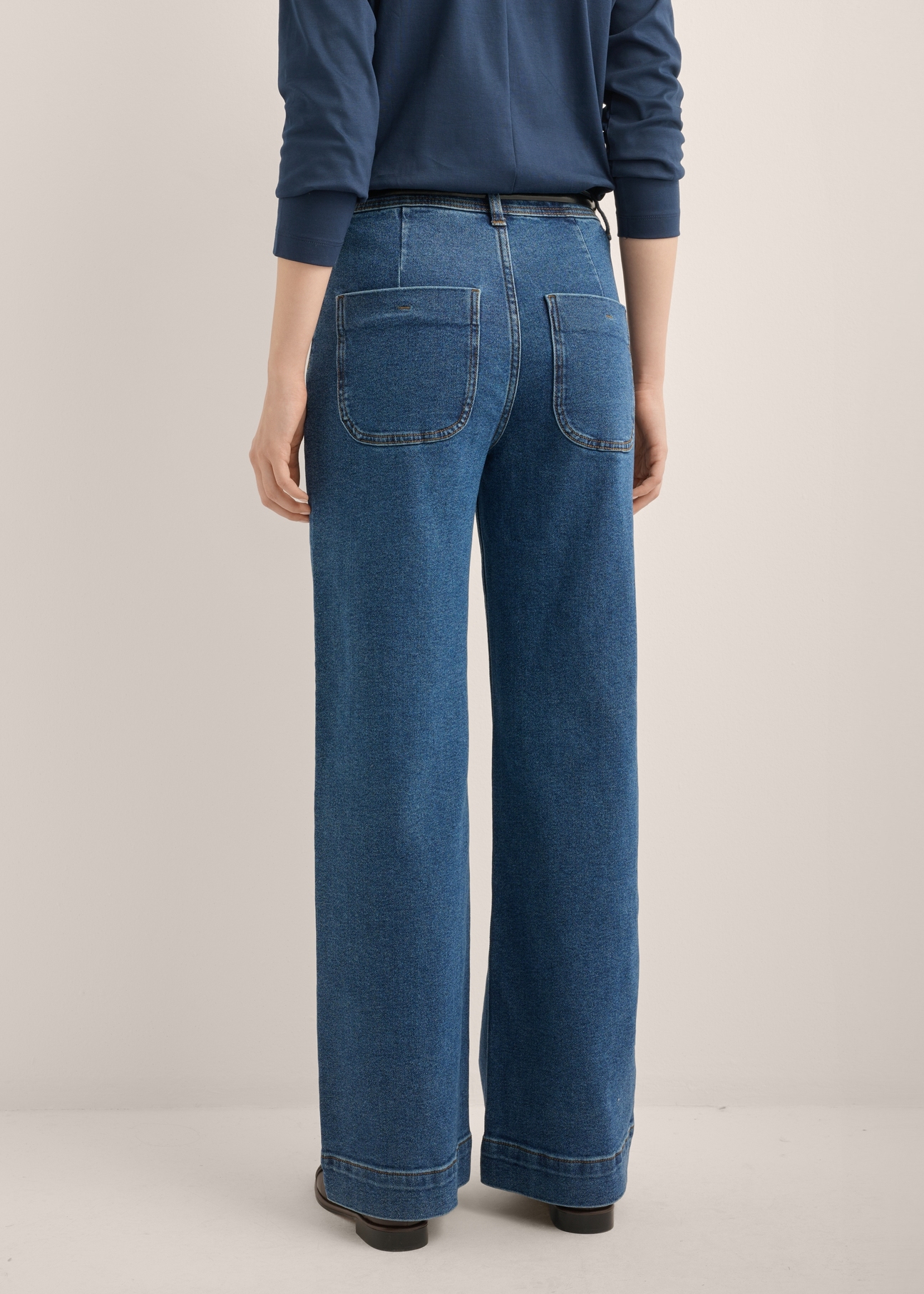 Damskie jeansy wide leg w kolorze ciemnogranatowym JEADT-0019-7D(Z26), widok produktu z tyłu na modelce. Widoczna połowa sylwetki.