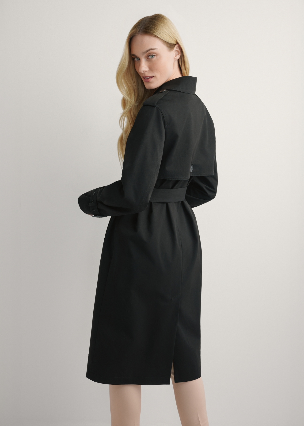 Długa czarna kurtka damska w formie płaszcza KURDT-0512-99(W25), widok produktu od tyłu na modelu, widoczna połowa sylwetki.