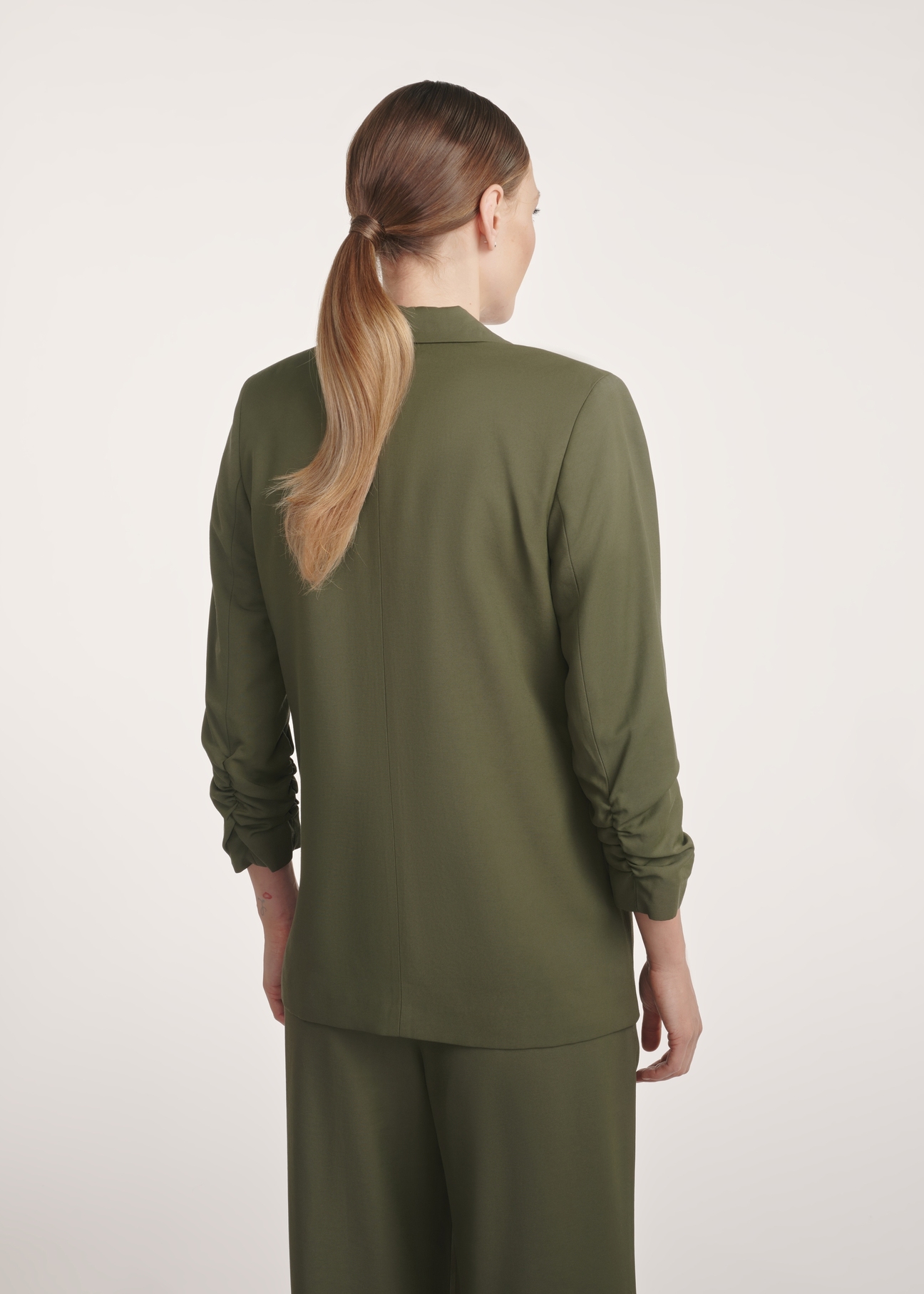 Marynarka damska w kolorze khaki ZAKDT-0043-55(Z25), widok produktu z tyłu na modelce. Widoczna połowa sylwetki.