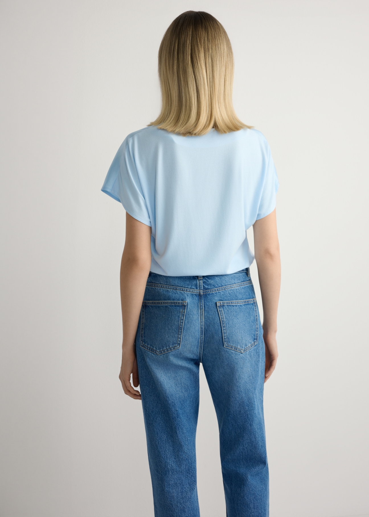 Jasnoniebieska bluzka damska BLUDT-0206-7A(W26), widok produktu z tyłu na modelce. Widoczna połowa sylwetki.