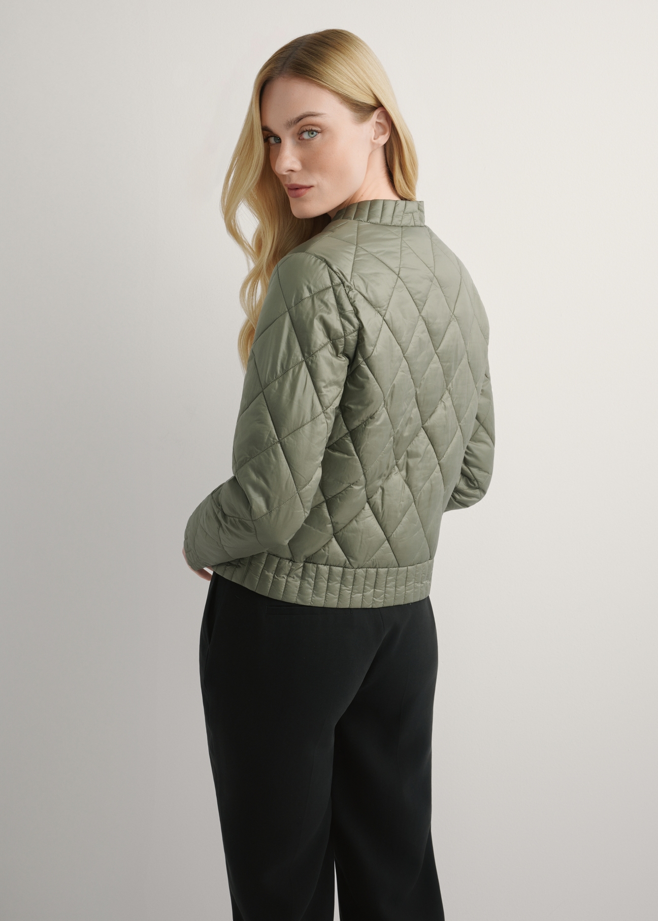 Przejściowa kurtka damska w kolorze khaki KURDT-0564A-55(W26), widok produktu z tyłu na modelce. Widoczna połowa sylwetki.