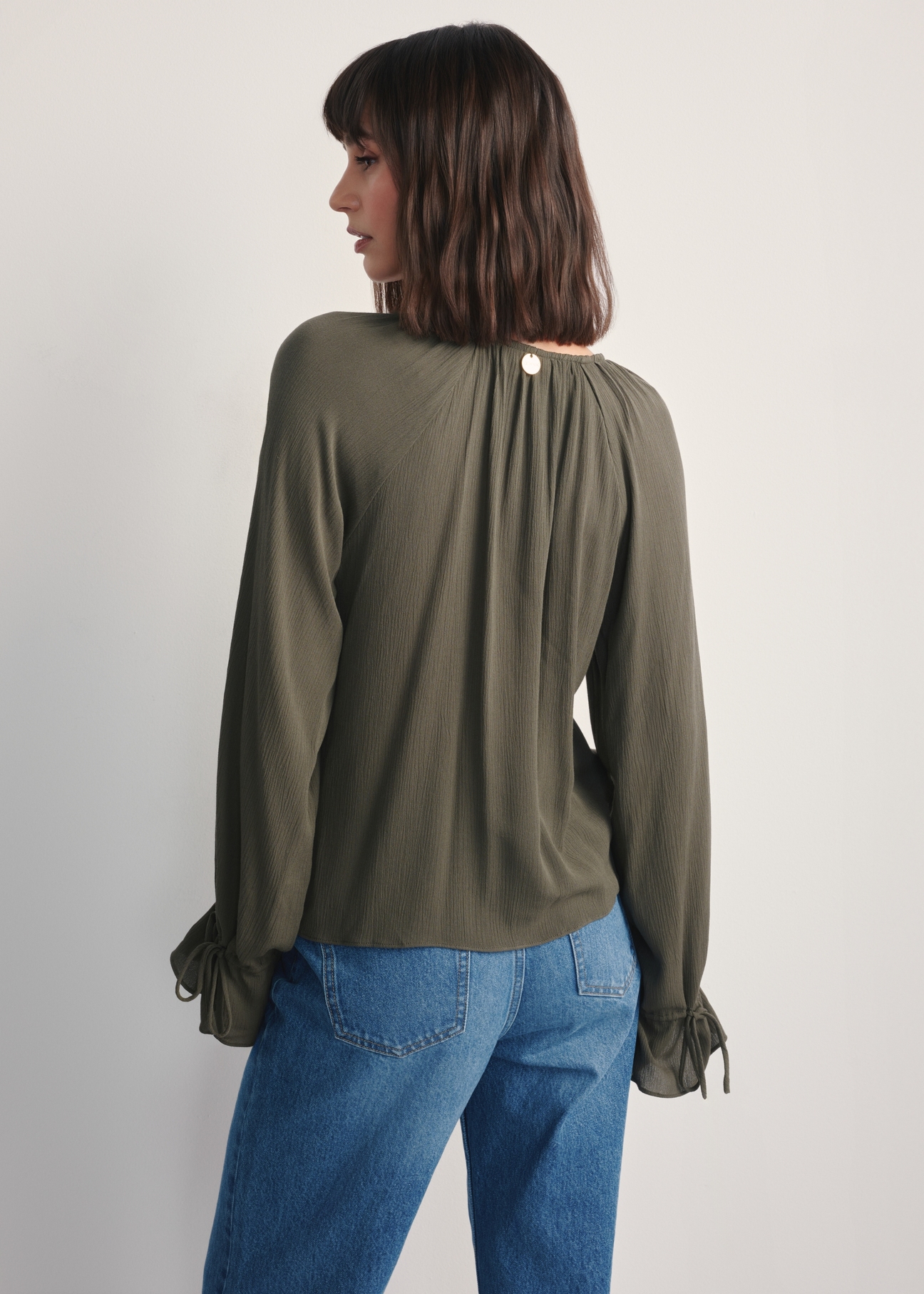 Bluzka damska w kolorze khaki BLUDT-0194-55(Z25), widok produktu tyłem na modelce, widoczna połowa sylwetki.