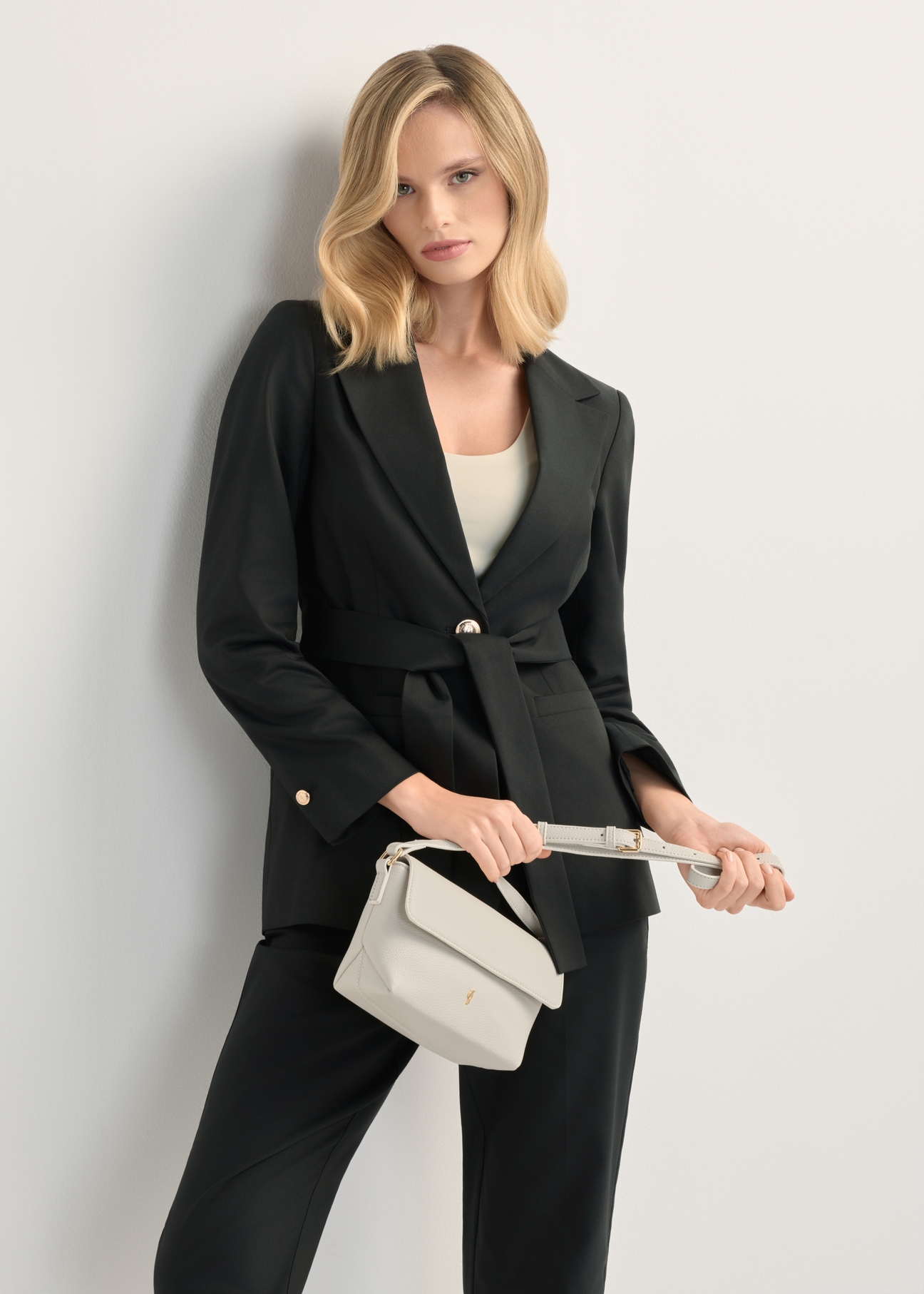 Kremowa mała torebka damska na ramię TOREC-0916-0B(W26), widok produktu z przodu w dłoni modelk. Widoczna połowa sylwetki.