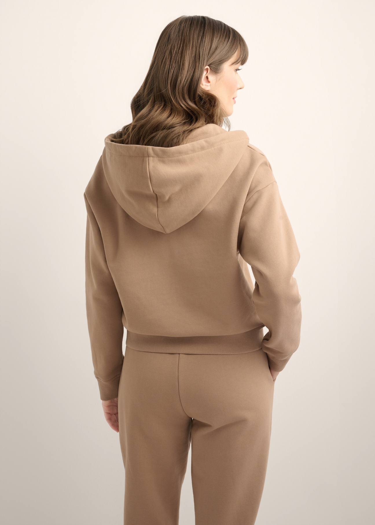 Rozpinana camelowa bluza damska z kapturem BLZDT-0122-1D(Z26), widok produktu od tyłu na modelce. Widoczna połowa sylwetki.