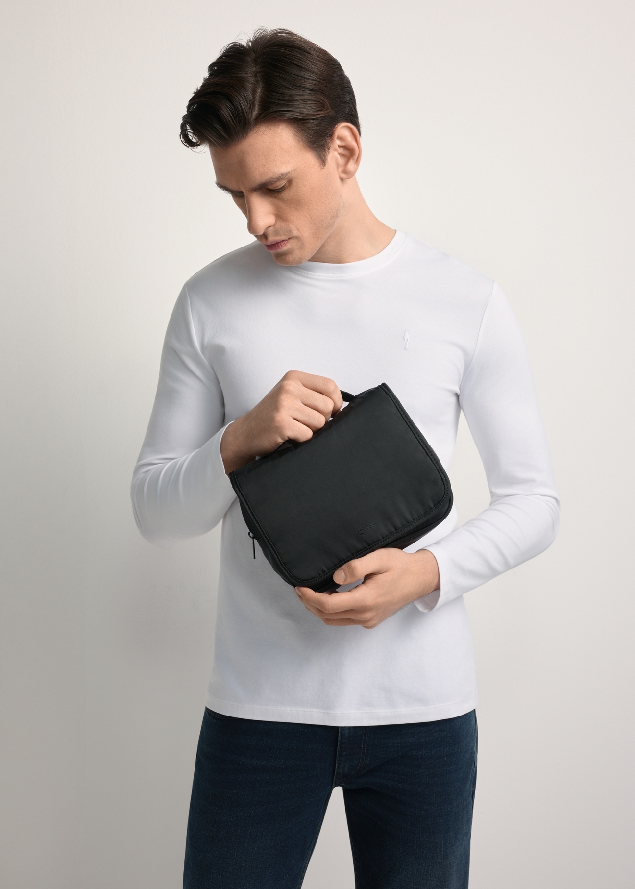 Kosmetyczka męska w kolorze czarnym TORMN-0370-99(Z25) - widok produktu z przodu, trzymanego przez modela w ręku, na jasnym tle. Widoczna połowa sylwetki. 