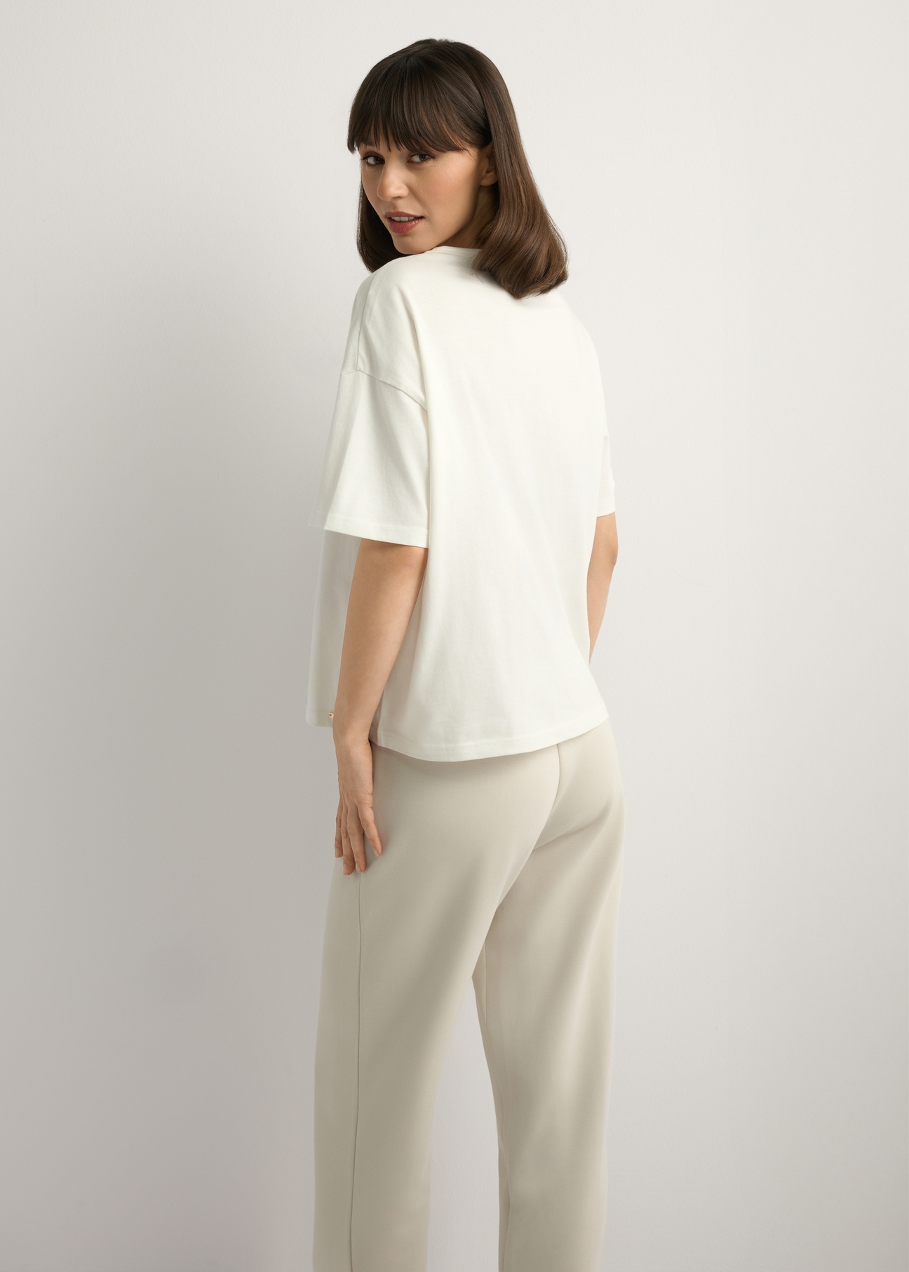 Kremowy T-shirt damski z nadrukiem TSHDT-0161-0B(W26), widok produktu z tyłu na modelce. Widoczna połowa sylwetki.