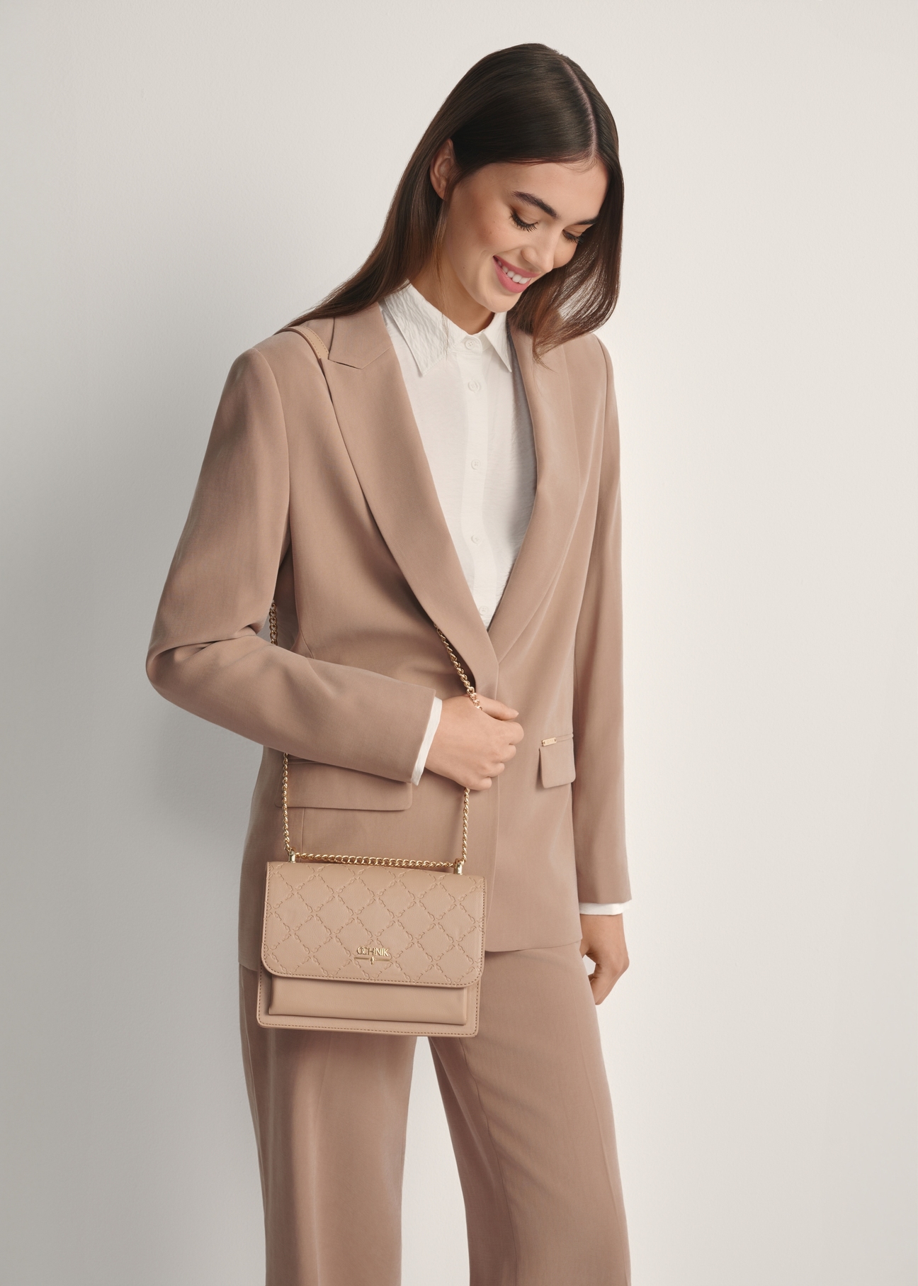 Beżowa torebka damska z monogramem TOREC-1155-1A(W26), widok produktu od przodu na modelce, widoczna połowa sylwetki.