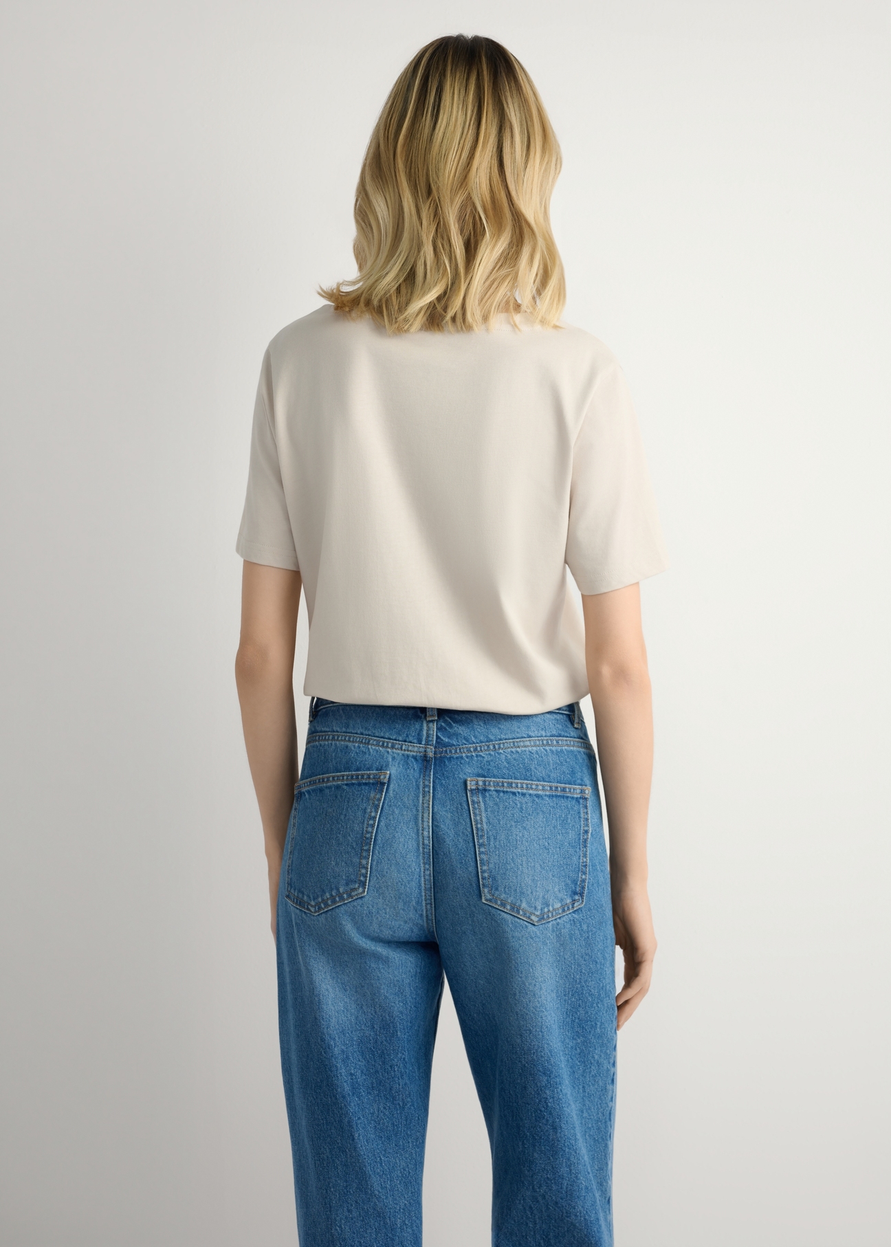 Jasnobeżowy T-shirt damski basic TSHDT-0120-1A(W26), widok produktu z tyłu na modelce. Widoczna połowa sylwetki.