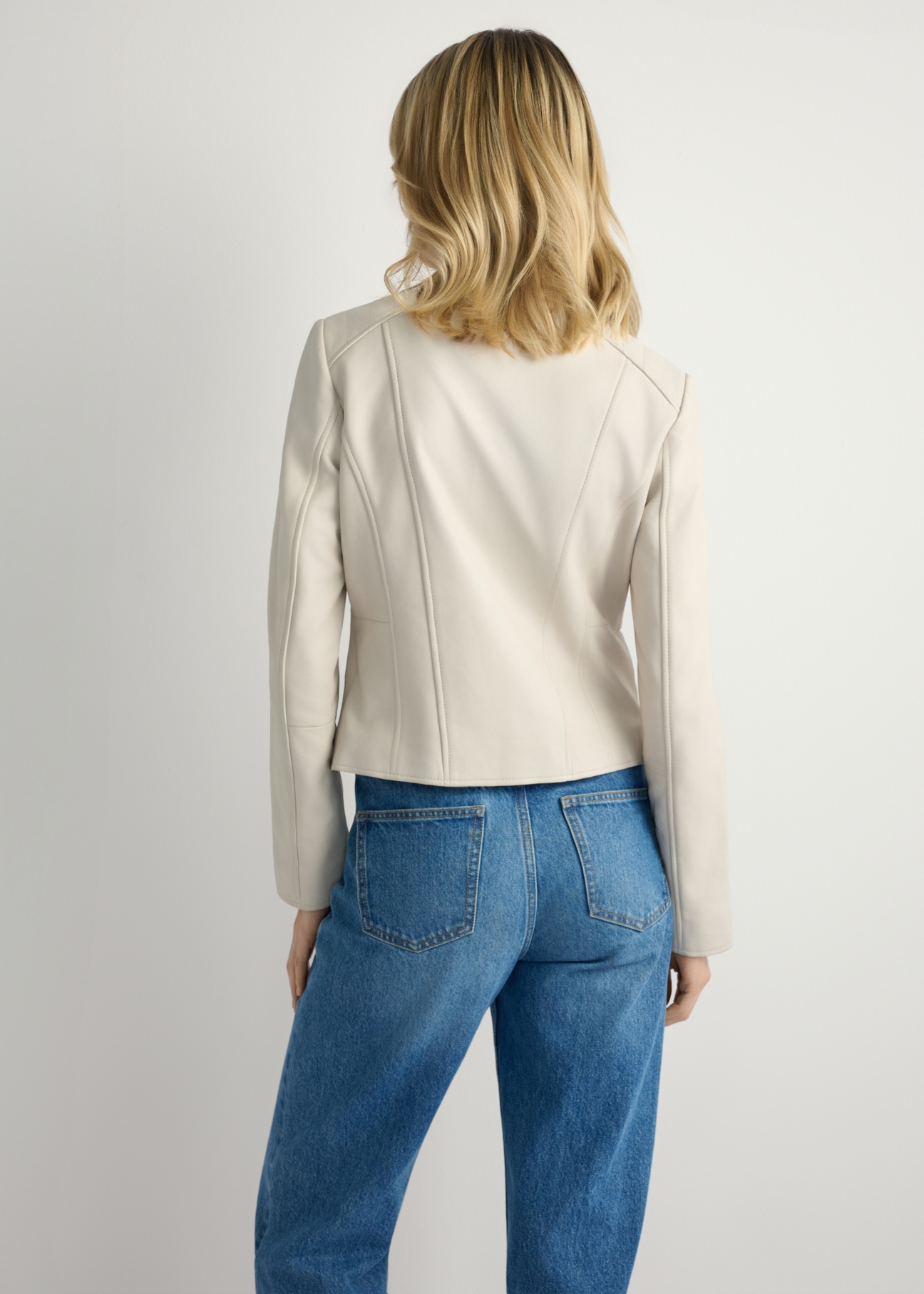 Skórzana krótka kurtka damska w kolorze beżu KURDS-0603-0B(W26) - widok produktu z tyłu, na modelce, na jasnym tle. Widoczna sylwetka do kolan.