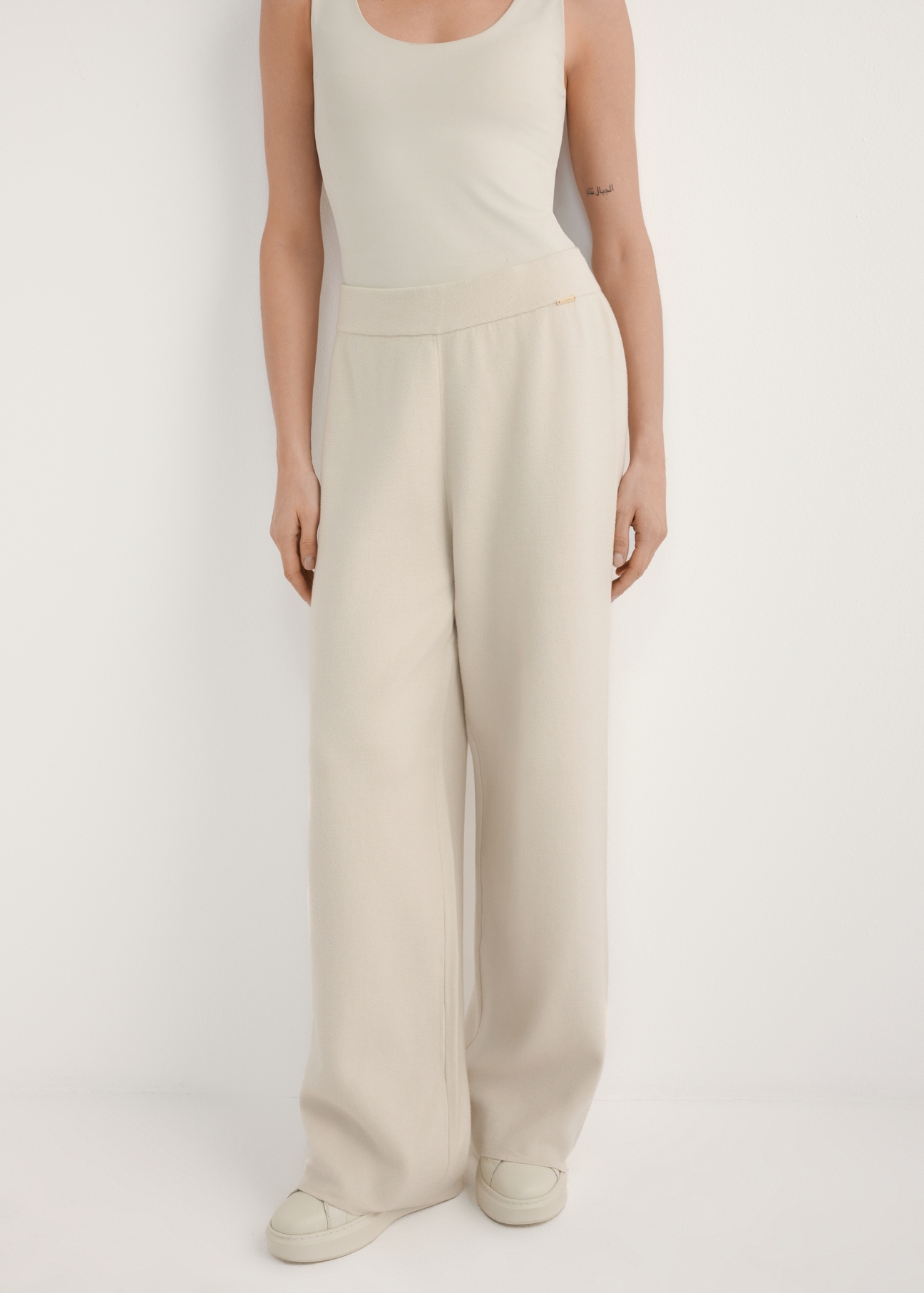 Beżowe szerokie spodnie damskie SPODT-0121-1A(W26), widok produktu z przodu na modelce. Widoczna połowa sylwetki.