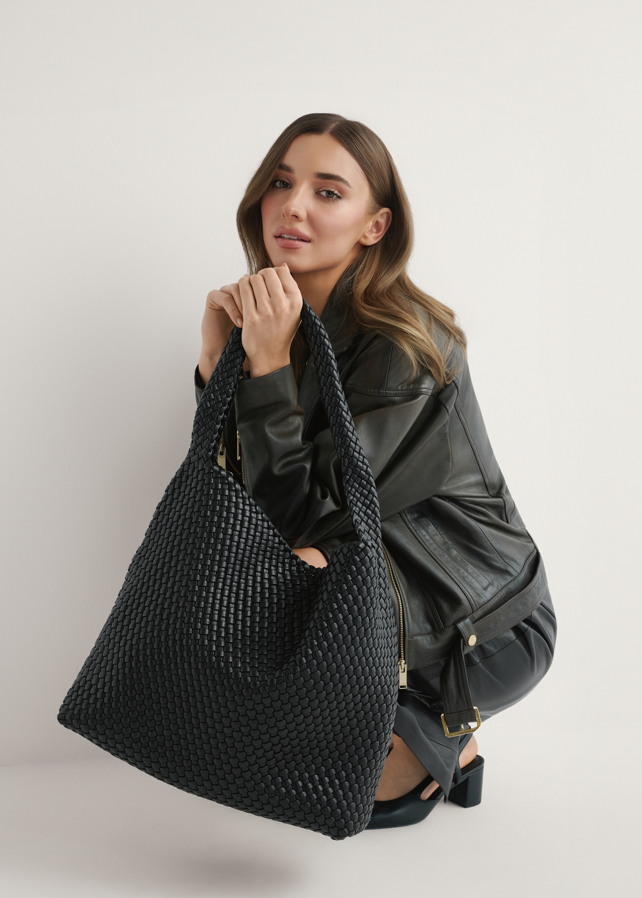 Czarna pleciona torebka damska TOREC-1147-99(W26) - widok produktu z przodu, trzymanego przez modelkę w ręku, na jasnym tle.