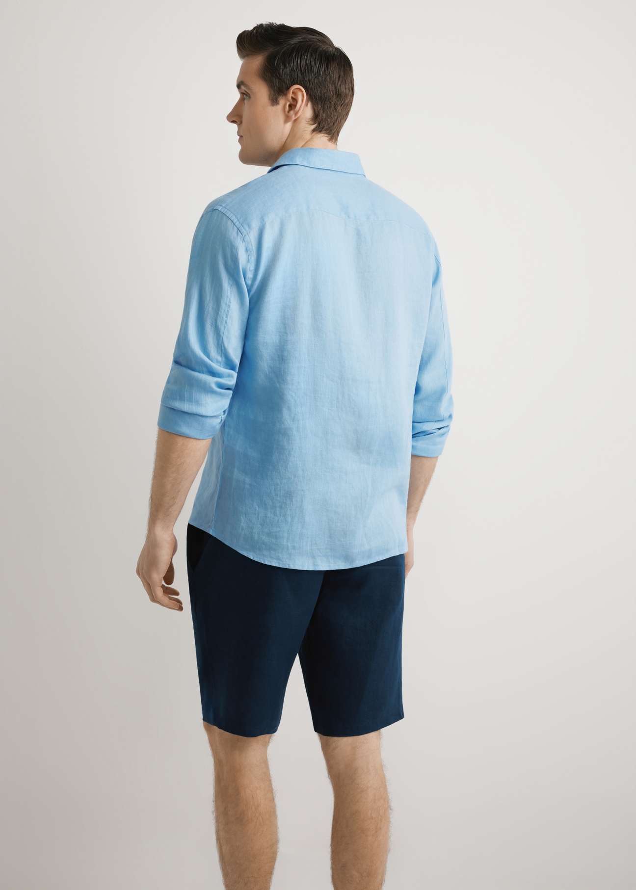 Niebieska lniana koszula męska KOSMT-0321A-7B(W26),  widok produktu z tyłu, na modelu, na jasnym tle. Widoczna połowa sylwetki. 