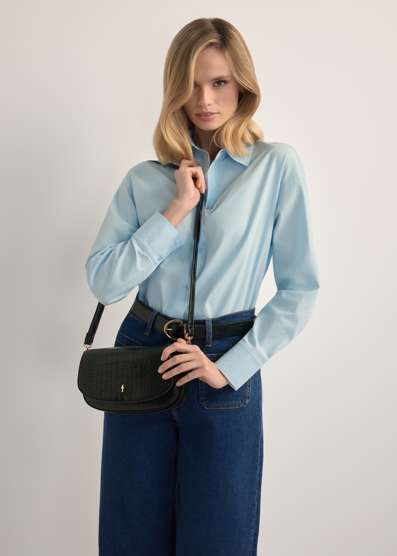 Mała czarna torebka listonoszka damska croco TOREC-1185-9G(W26), widok produktu na ramieniu modelki. Widoczna połowa sylwetki.