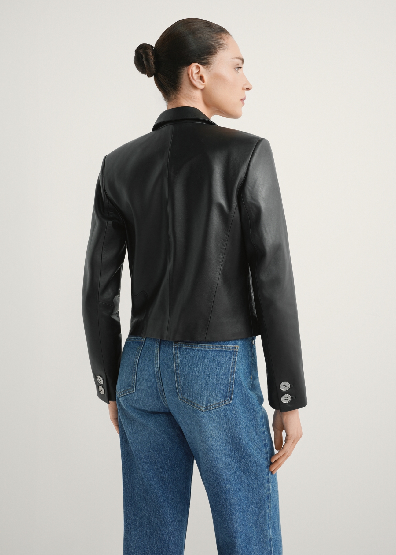 Krótka skórzana marynarka damska KURDS-0522-99(W26) - widok produktu z tyłu, na modelce, na jasnym tle. Widoczna połowa sylwetki.