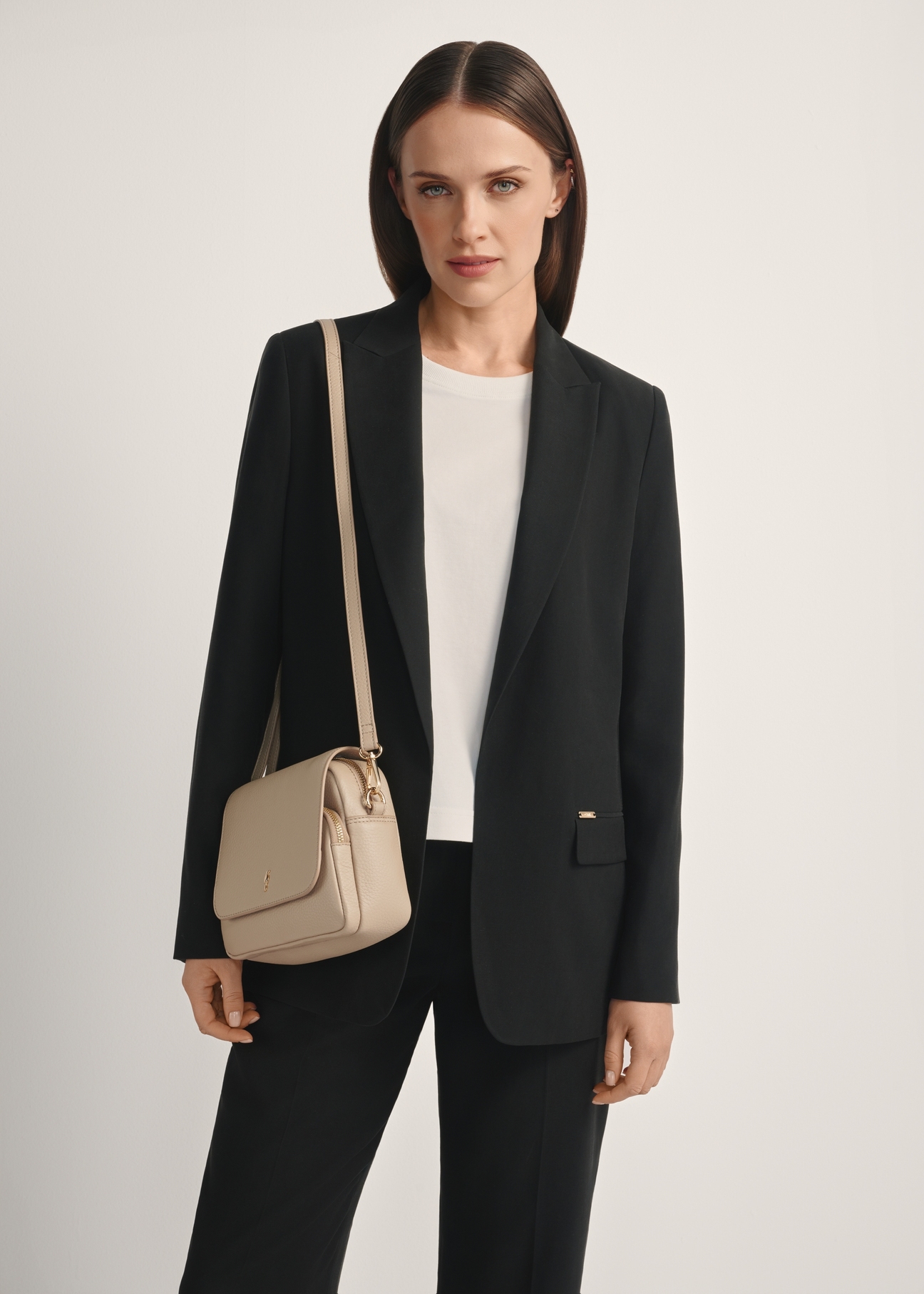 Beżowa skórzana torebka listonoszka damska TORES-0958E-1B(W26), widok produktu skosem na modelce, widoczna połowa sylwetki.