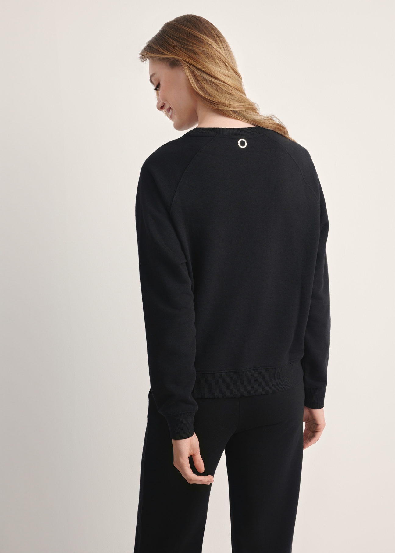 Czarna bluza damska BLZDT-0114-99(Z25), produkt widoczny od tyłu na modelce, widoczne pół sylwetki.
