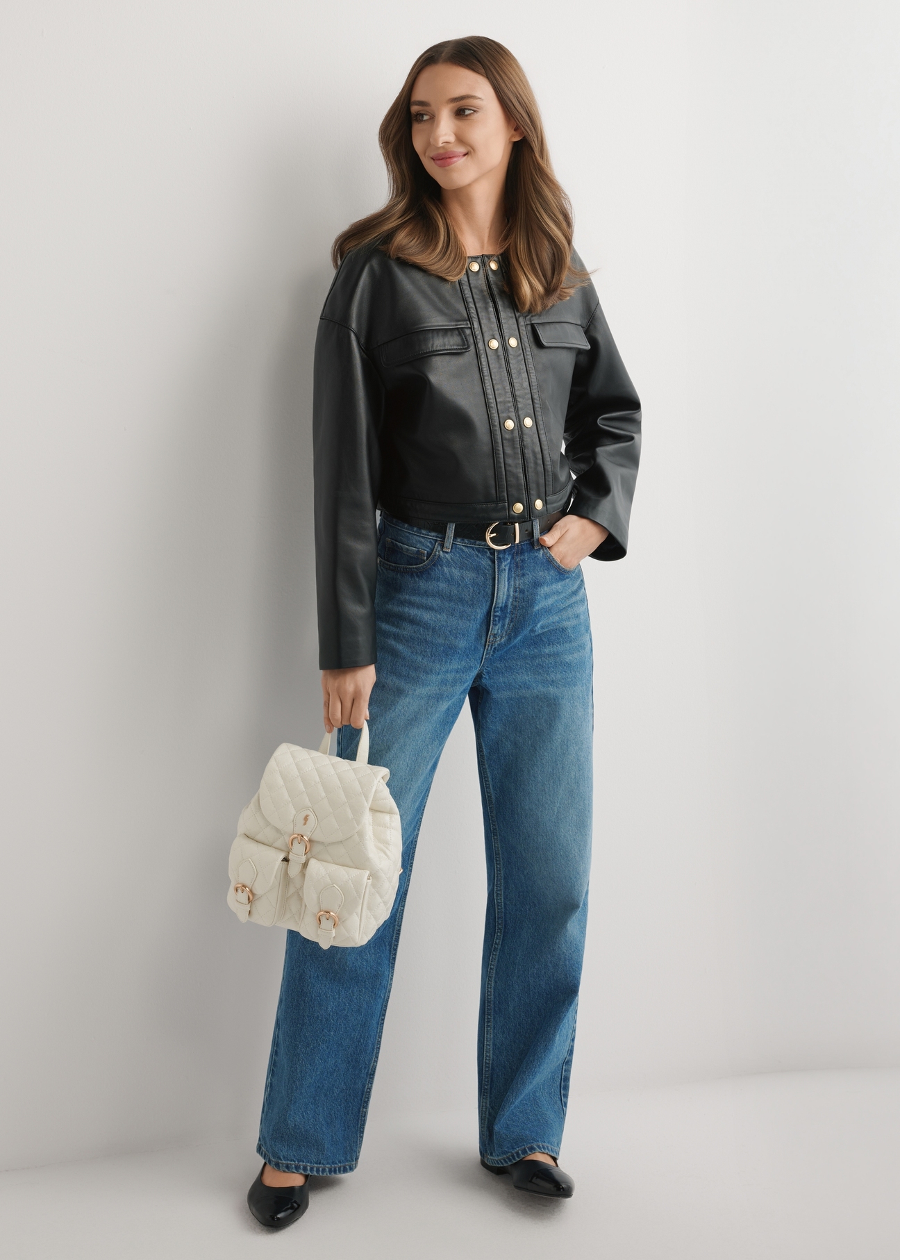 Kremowy pikowany plecak damski TOREC-1195-0A(W26) - widok produktu z przodu, trzymanego przez modelkę w ręku, na jasnym tle. Widoczna cała sylwetka. 