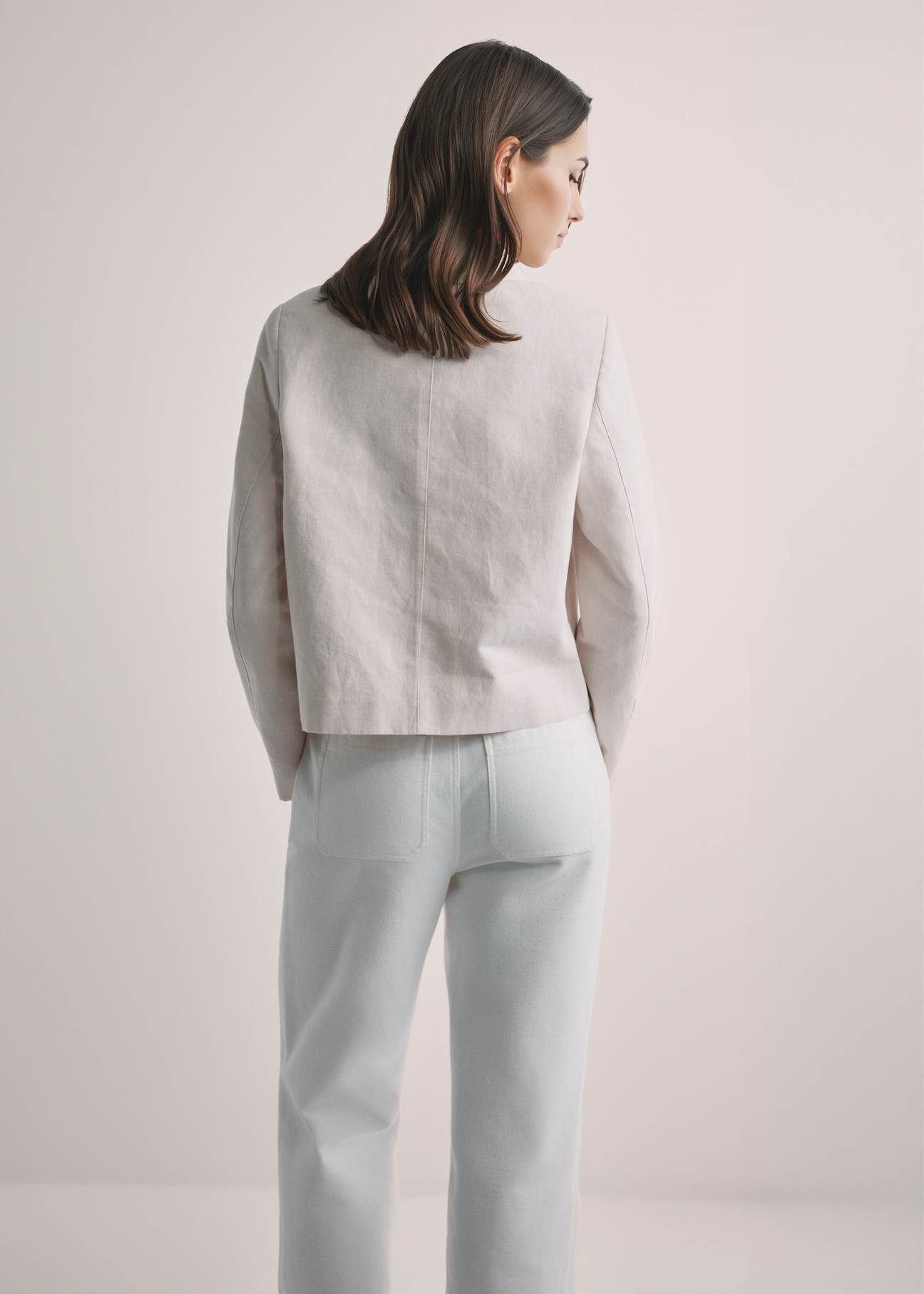 Jasnobeżowa kurtka damska z lnem KURDT-0652-1A(W26), widok produktu z tyłu na modelce. Widoczna połowa sylwetki.