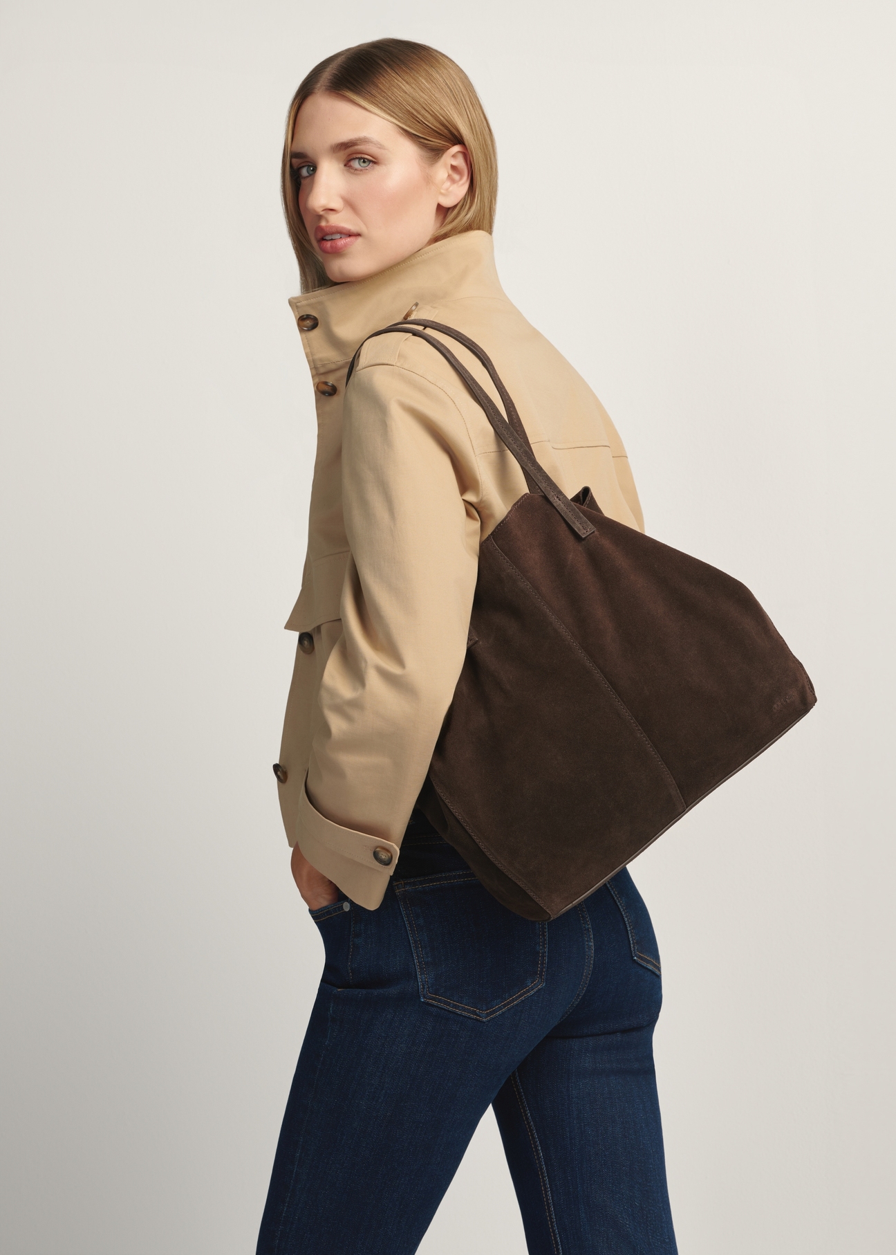 Skórzana ciemnobrązowa torebka damska TORES-1252-1I(W26) - widok produktu po skosie, na modelce, na białym tle. Widoczna sylwetka do kolan.