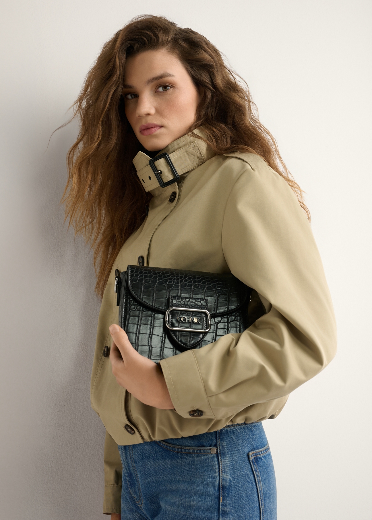 Czarna listonoszka damska croco TOREC-0880-9G(W26) - widok produktu z przodu, trzymanego przez modelkę w ręku, na jasnym tle. Widoczna połowa sylwetki. 