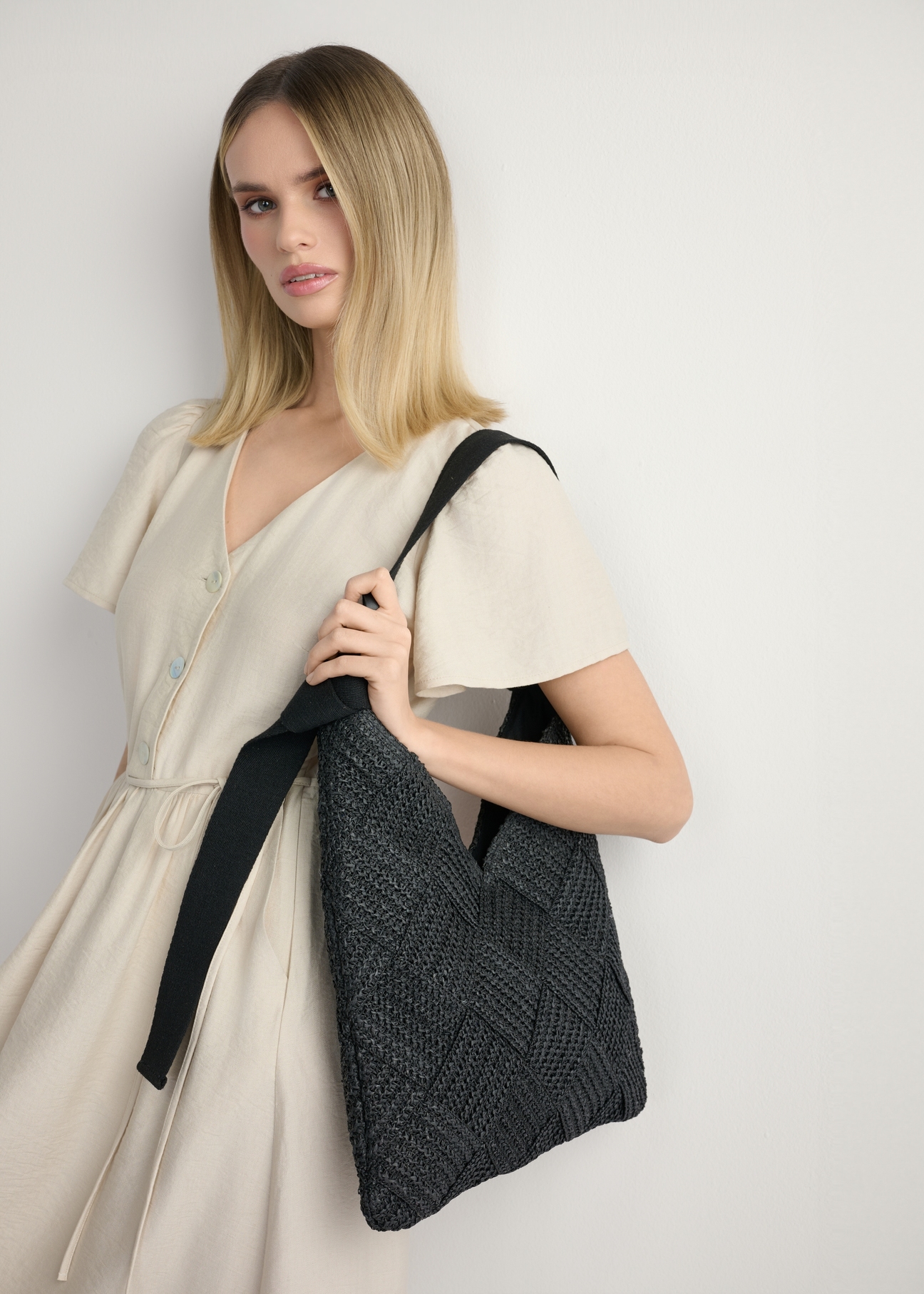 Czarna torebka damska z naturalnego włókna TOREC-1039-99(W26) - widok produktu po skosie, na modelce, na jasnym tle. Widoczna sylwetka do kolan. 