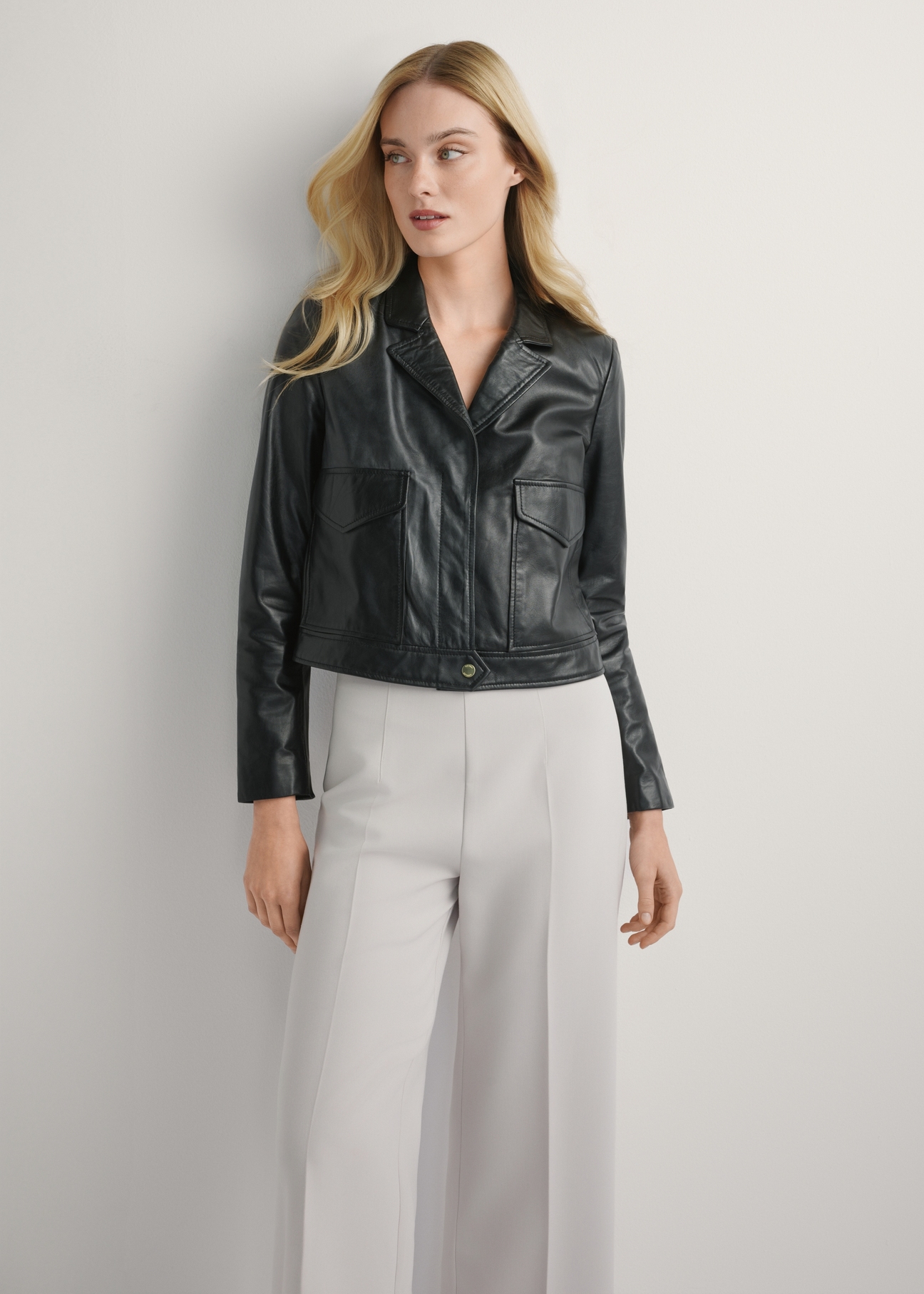 Czarna skórzana krótka kurtka damska KURDS-0471-99(W26), widok produktu z przodu na modelce. Widoczna połowa sylwetki.