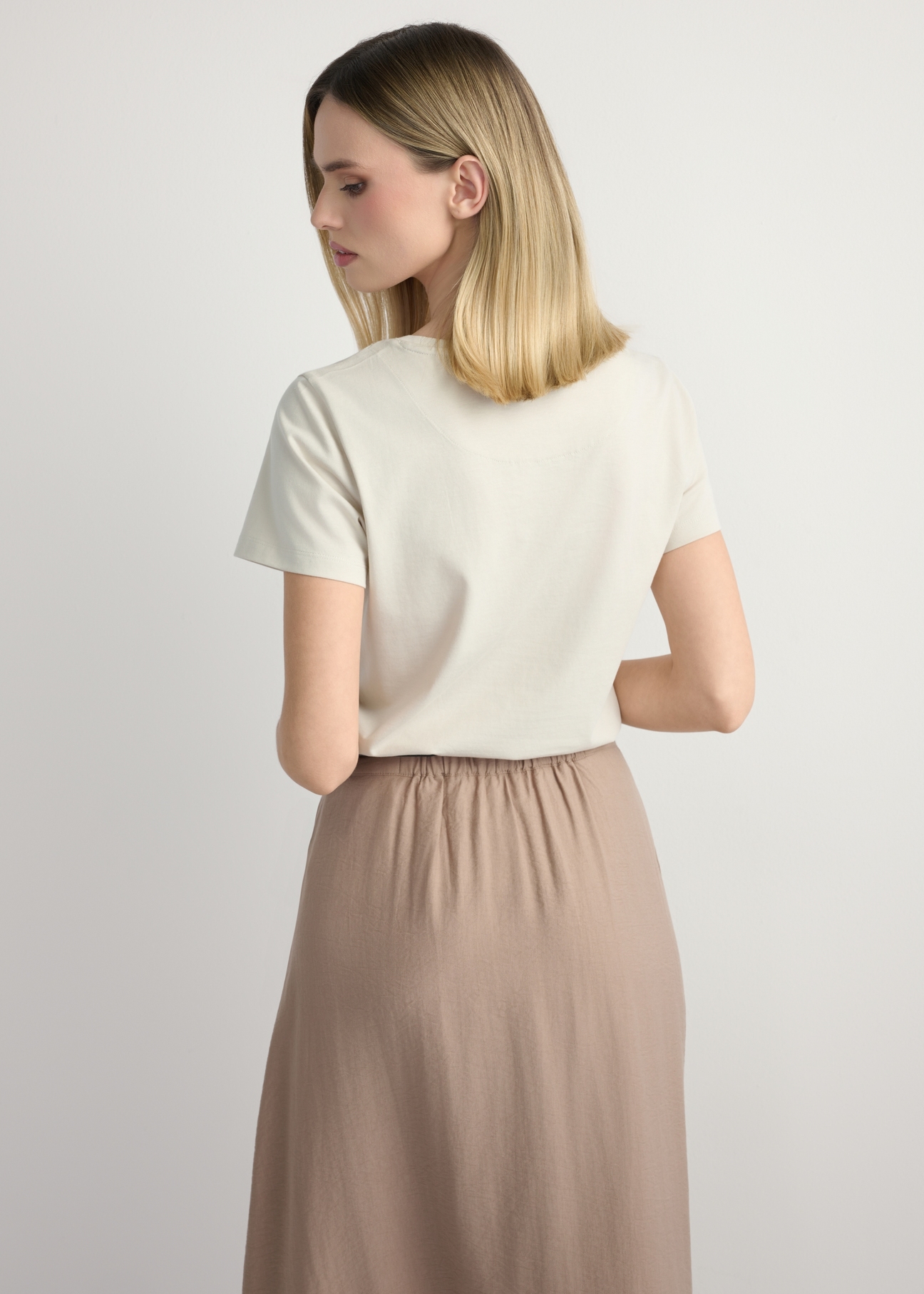 Jasnobeżowy T-shirt damski z logo TSHDT-0157-1A(W26), widok produktu z tyłu na modelce. Widoczna połowa sylwetki.