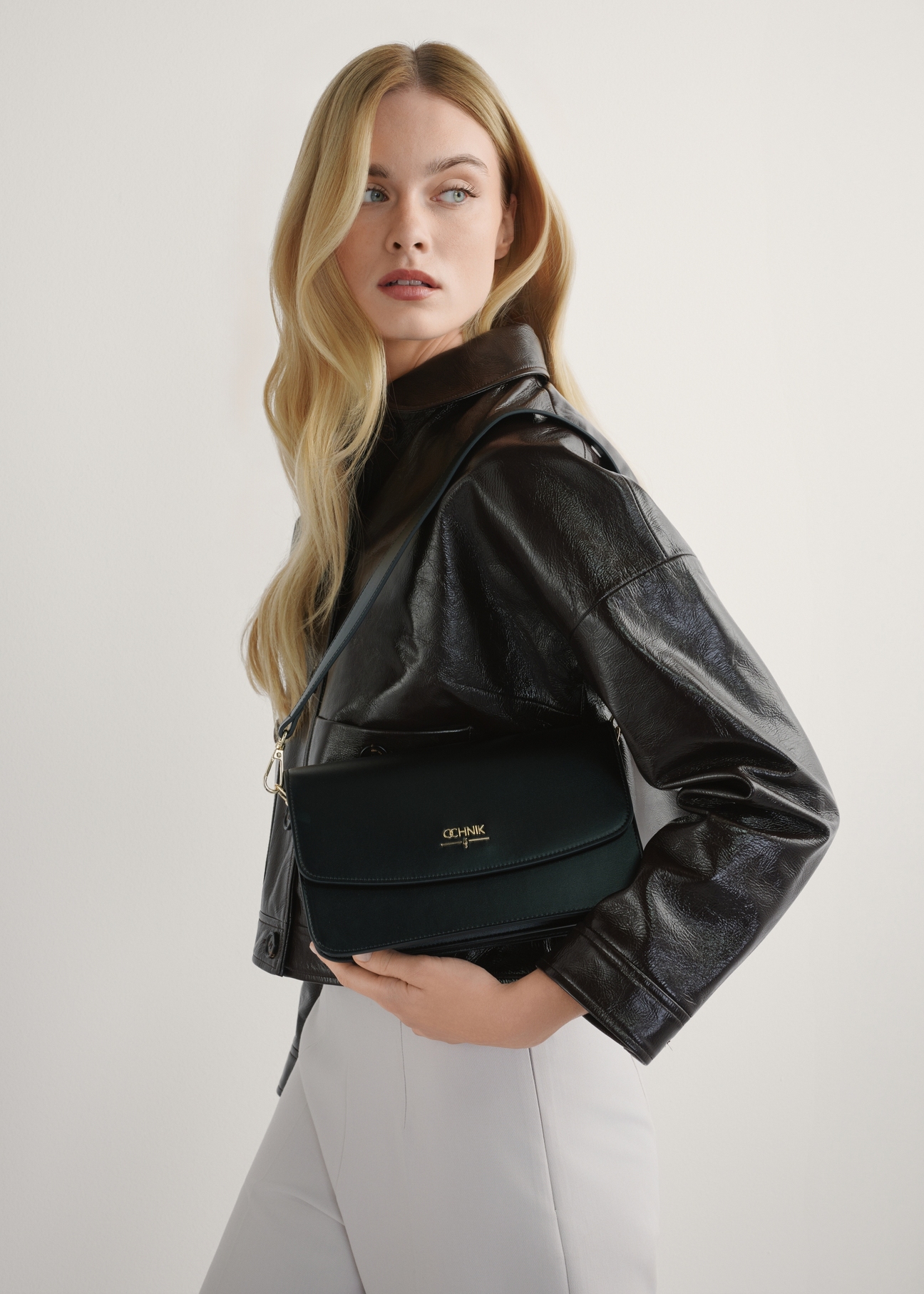 Czarna torebka damska z imitacji skóry TOREC-1081-99(W26), widok produktu w rękach modelki. Widoczna połowa sylwetki.