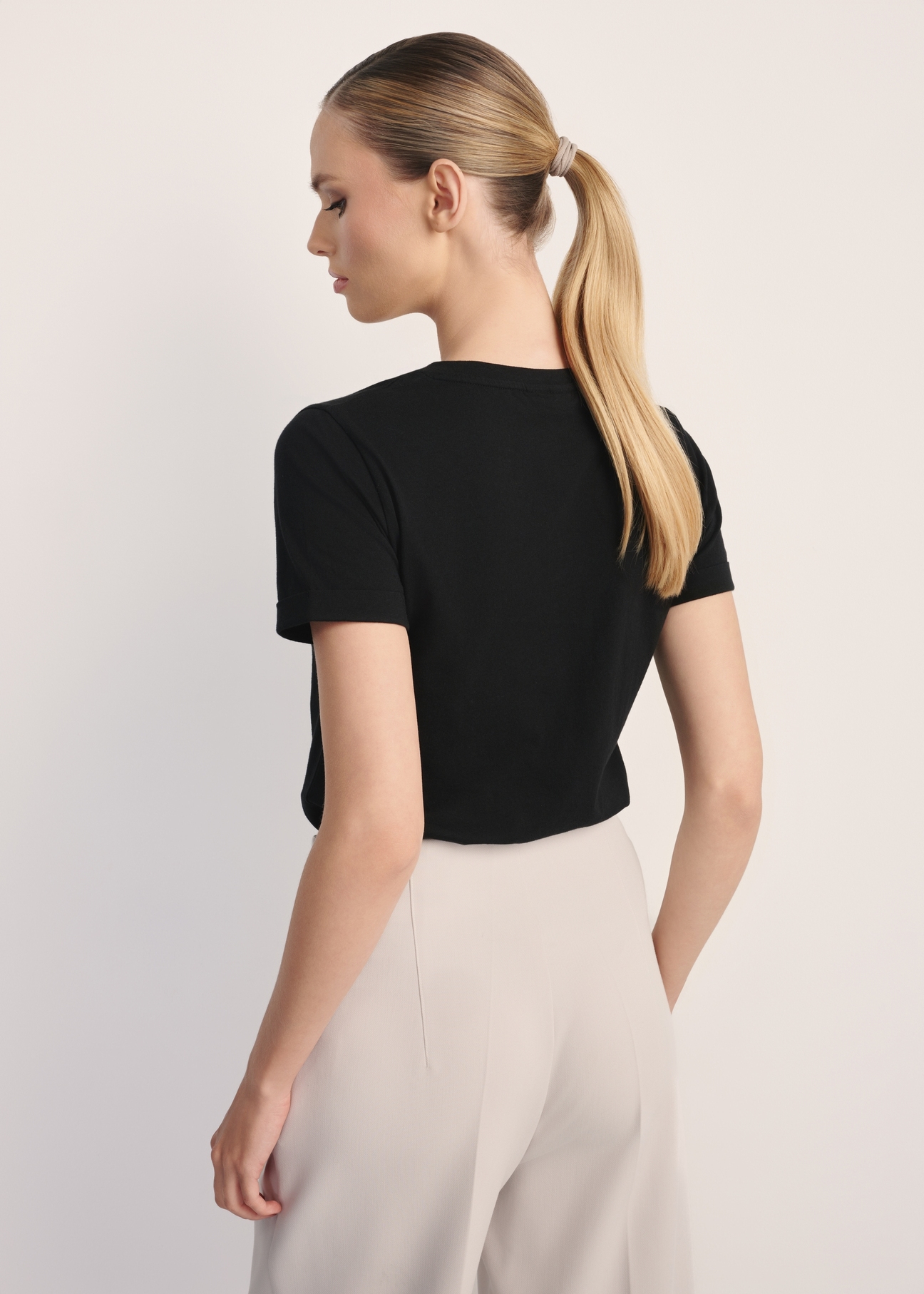 Czarny T-shirt damski w serek TSHDT-0118A-99(Z25), widok produktu z tyłu na modelce. Widoczna połowa sylwetki.