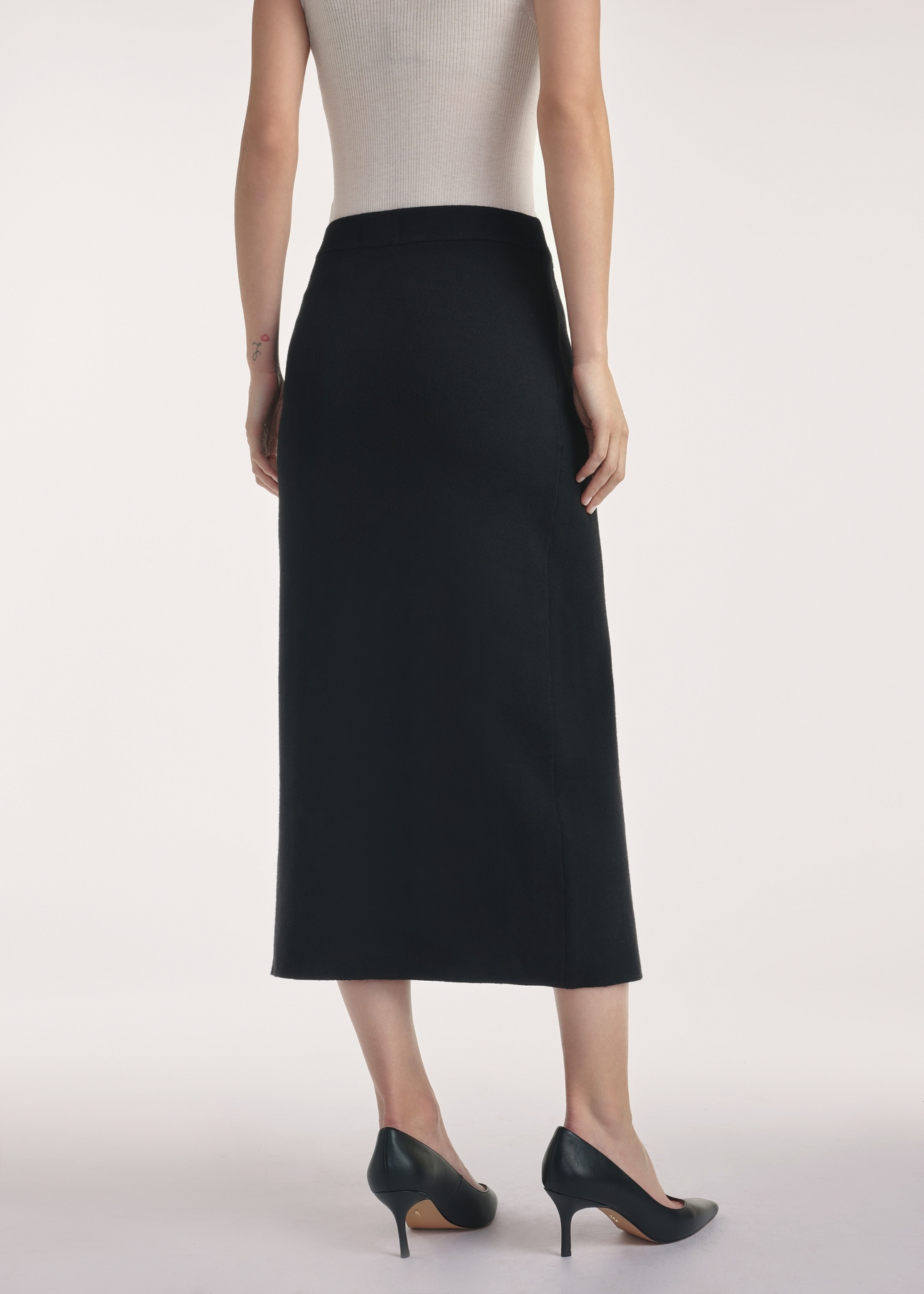 Czarna spódnica midi SPCDT-0114-99(Z25), widok produktu z tyłu na modelce, widoczne pół sylwetki.