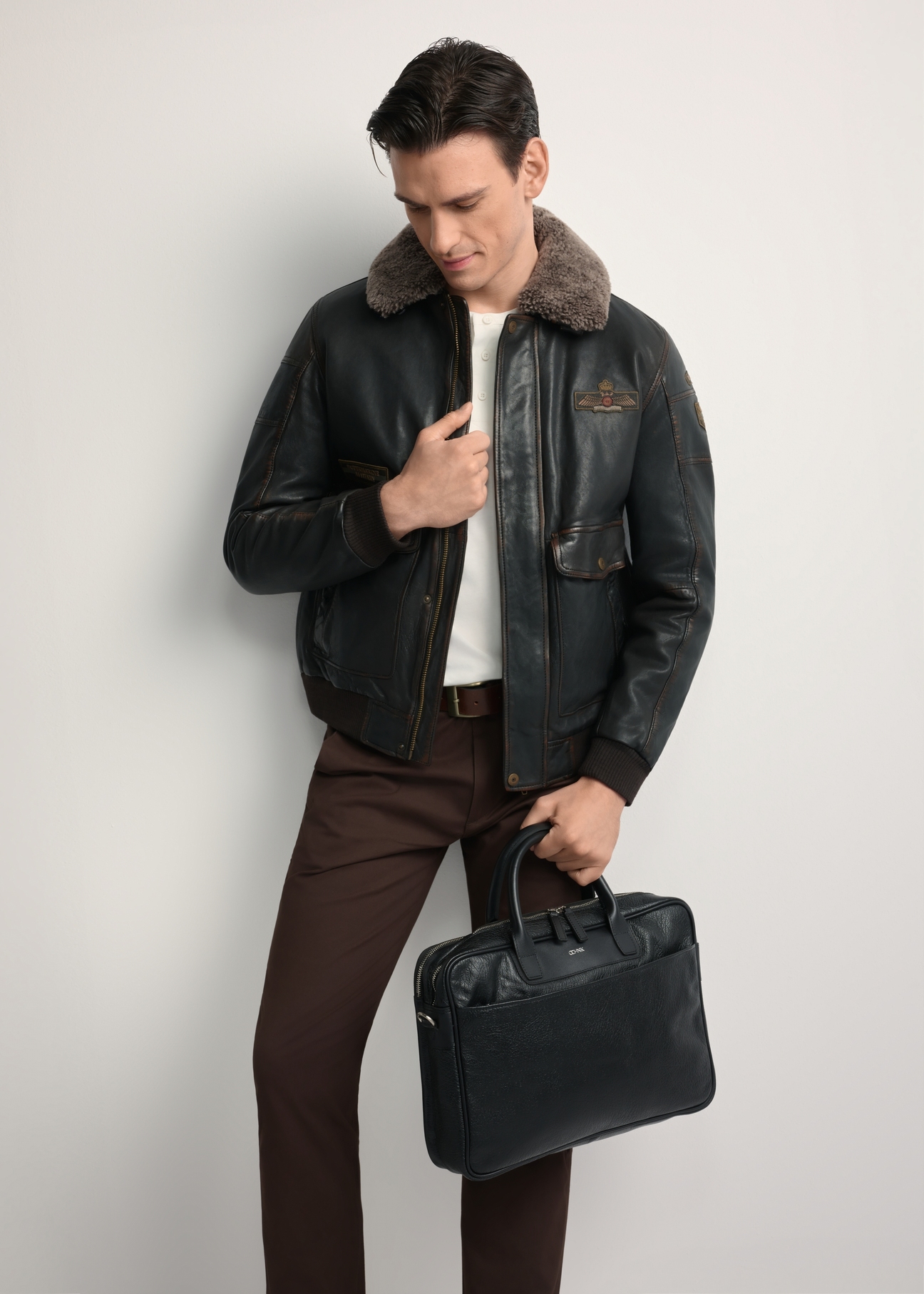 Czarna skórzana torba męska TORMS-0299A-99(Z25)- widok produktu po skosie, trzymanego przez modela w ręku, na białym tle. Widoczna cała sylwetka. 