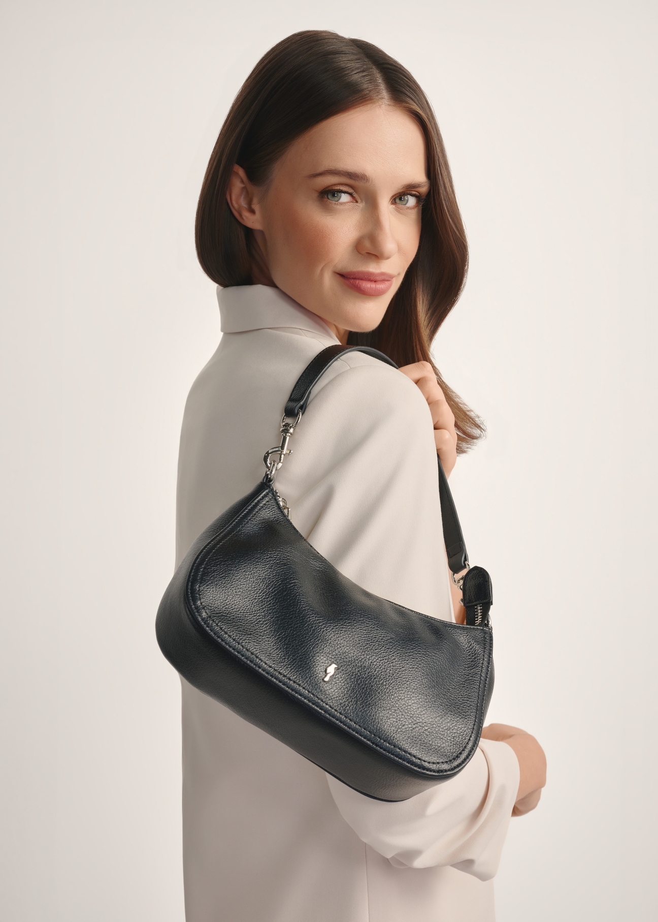 Mała czarna torebka damska TOREC-1134-99(W26) - widok produktu od frontu, na modelce, na białym tle. Widoczna połowa sylwetki.