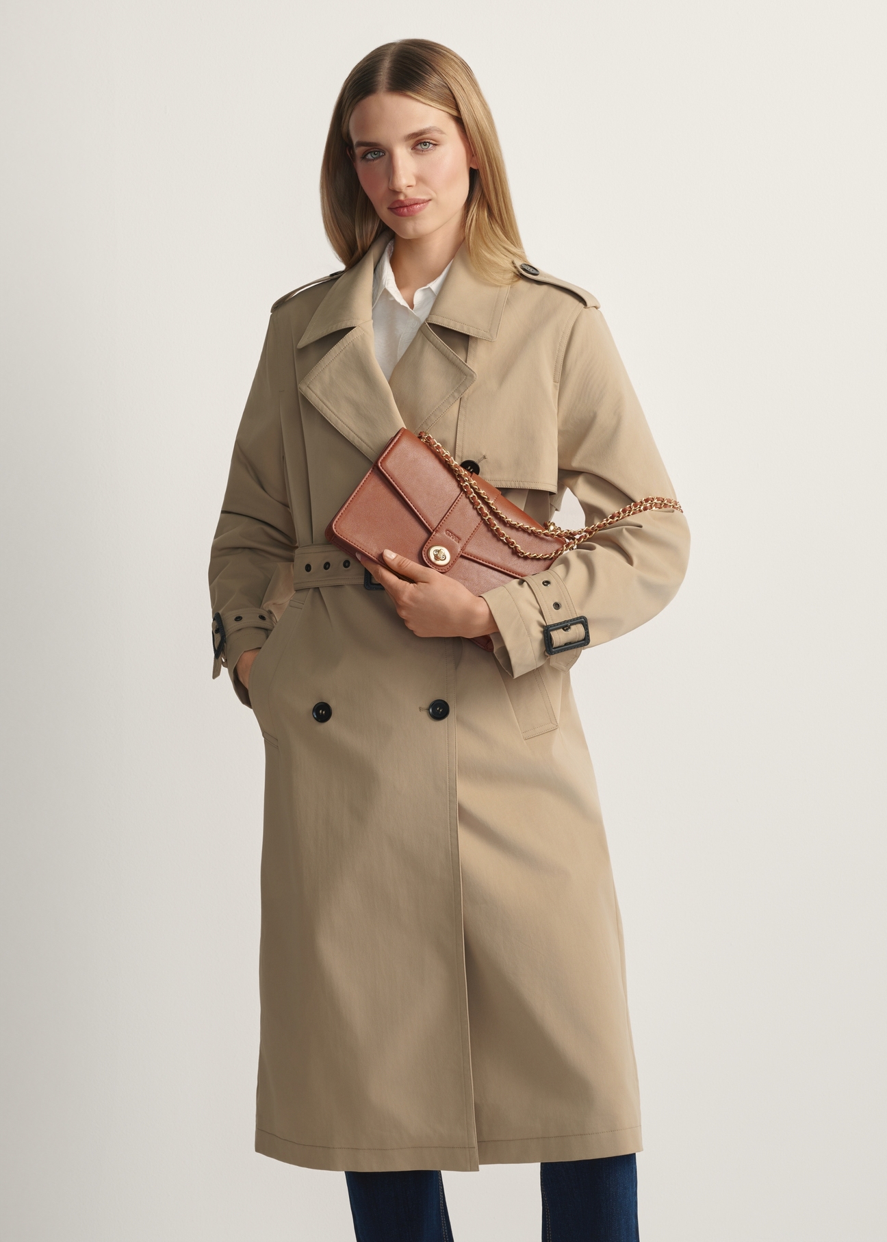 Brązowa torebka listonoszka damska TOREC-1137-1F(W26)- widok produktu z przodu, na modelce, na jasnym tle. Widoczna sylwetka do kolana.