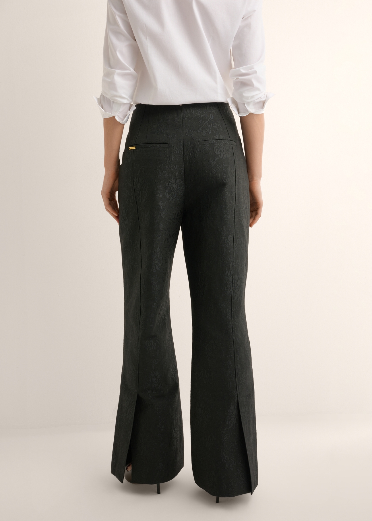 Czarne spodnie wide leg w kwiaty SPODT-0127-99(Z26), widok produktu z tyłu na modelce. Widoczna połowa sylwetki.