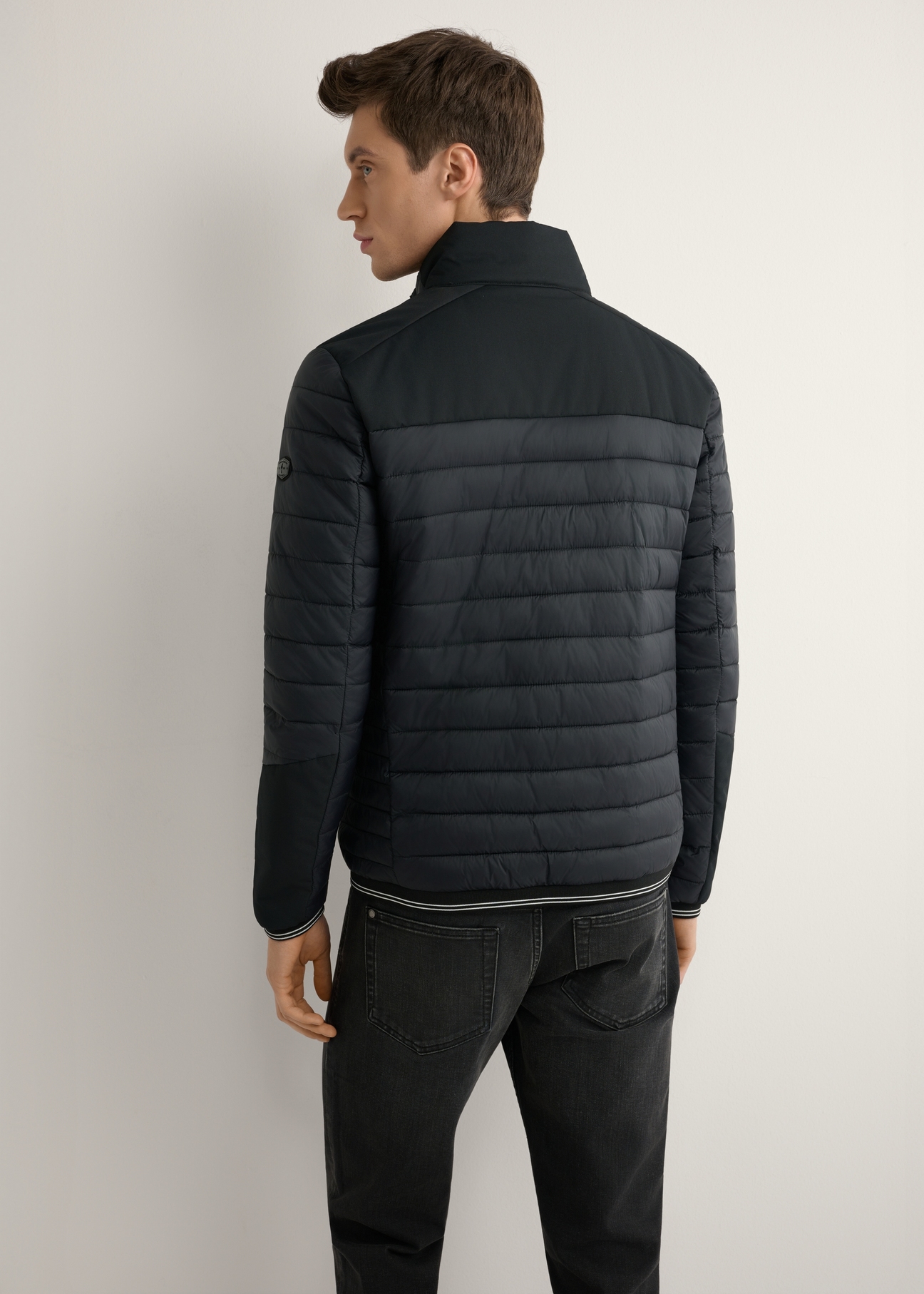 Czarna kurtka męska przejściowa KURMT-0358A-99(W26) - widok produktu z tyłu na modelu, na jasnym tle. Widoczna połowa sylwetki.