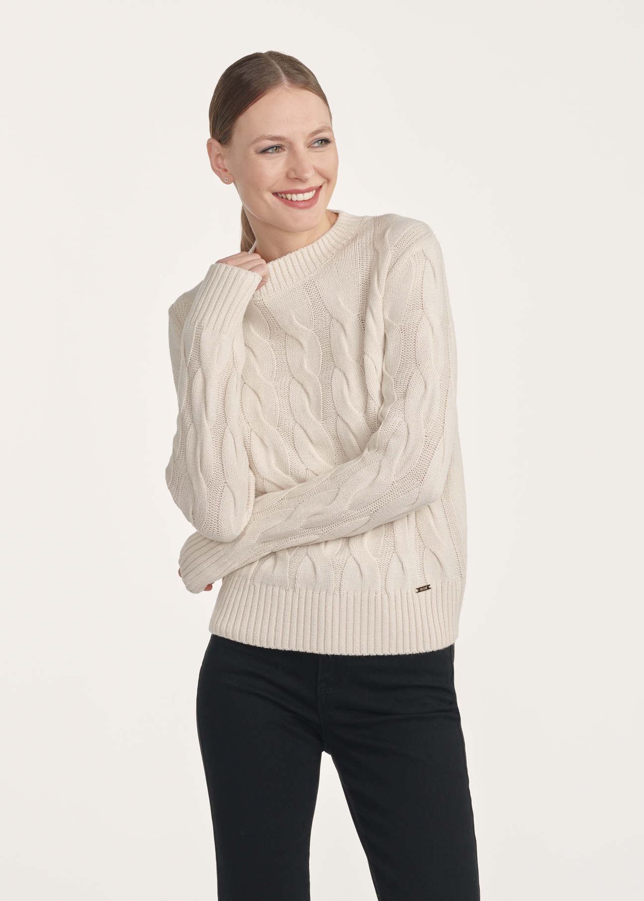 Jasnobeżowy sweter damski z ozdobnym splotem SWEDT-0210-80(Z25), widok produktu z przodu na modelce. Widoczna połowa sylwetki.