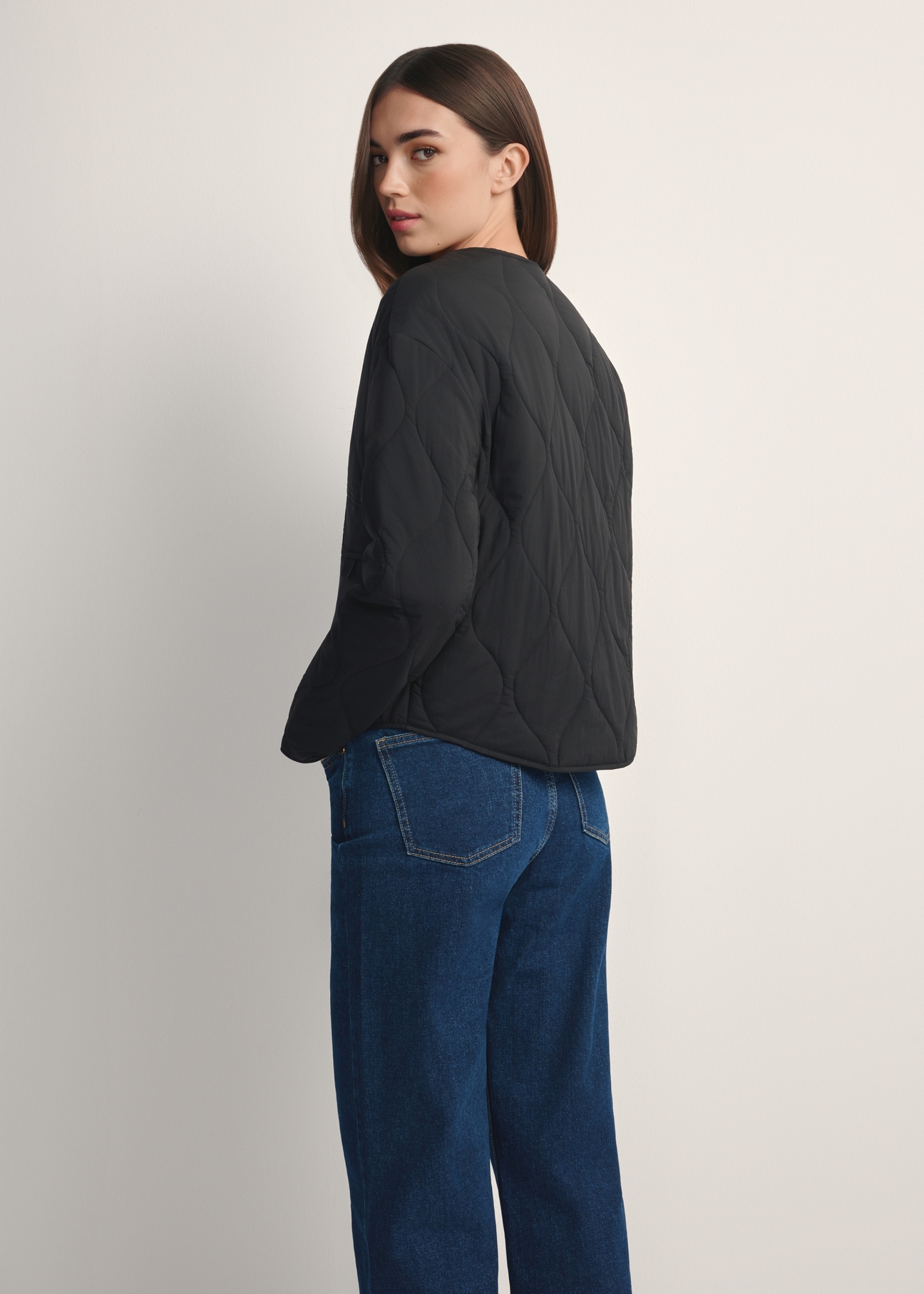 Czarna przejściowa kurtka damska z nylonu KURDT-0656-99(W26), widok produktu od tyłu na modelce, widoczna połowa sylwetki.