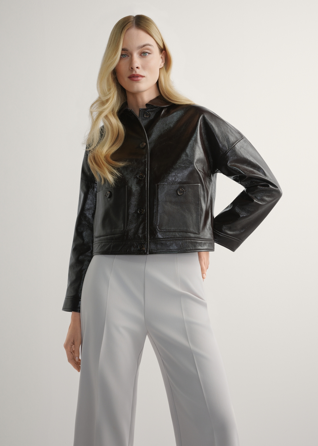 Brązowa skórzana krótka kurtka damska KURDS-0593-1I(W26) - widok produktu z przodu, na modelce, na jasnym tle. Widoczna sylwetka do kolan. 