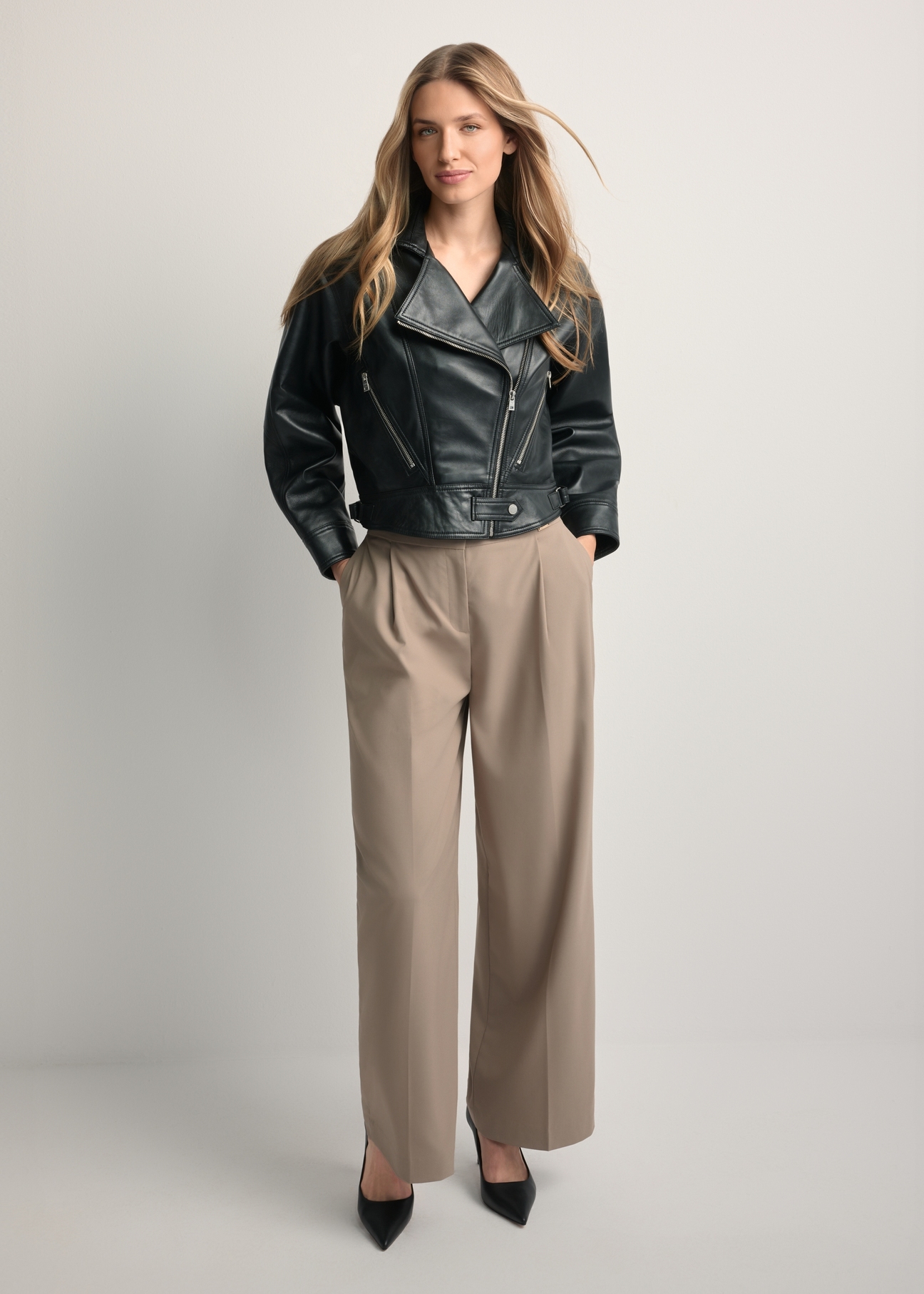 Krótka czarna skórzana kurtka damska KURDS-0607-99(W26) - widok produktu z przodu na modelce, na jasnym tle. Widoczna cała sylwetka.