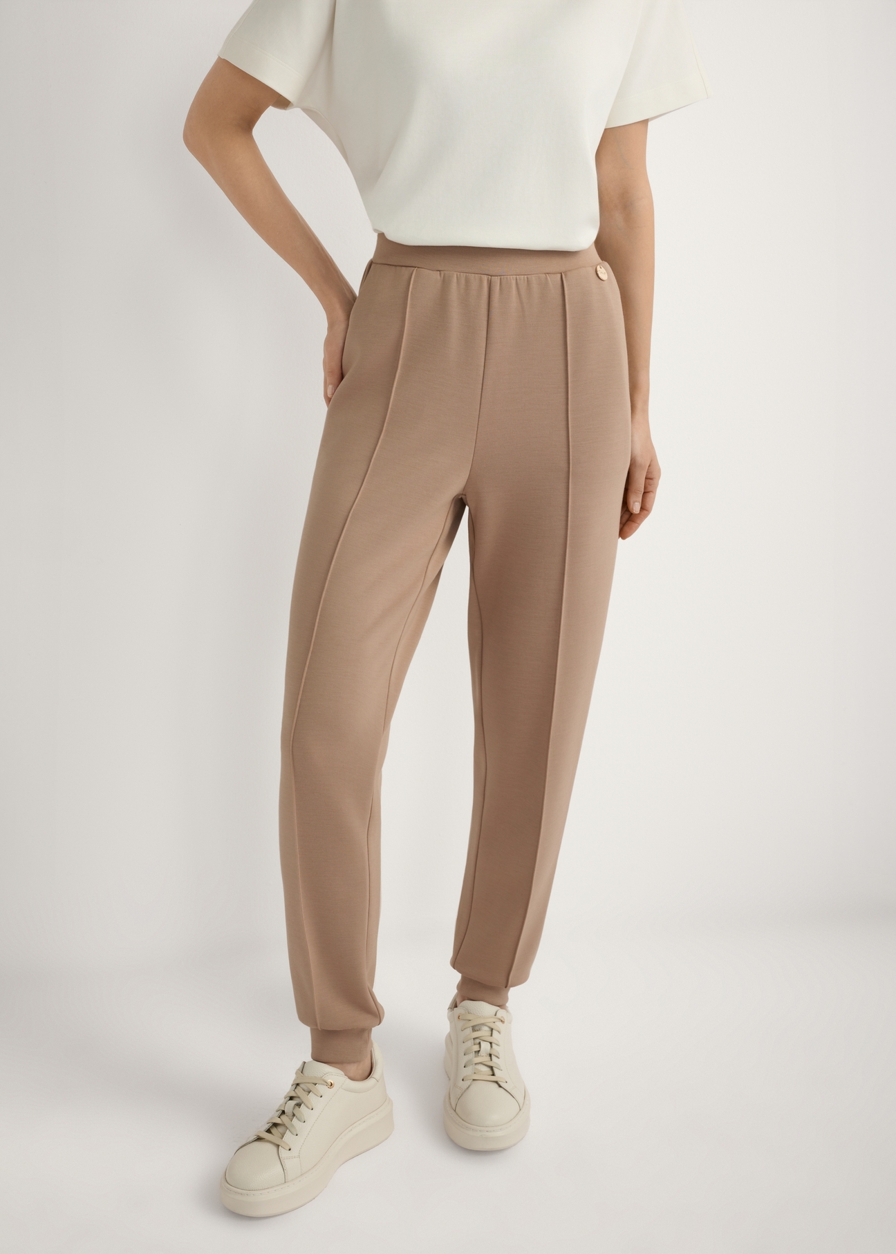 Kamelowe spodnie ze zwężaną nogawką SPODT-0104A-1D(W26), widok produktu z przodu na modelce. Widoczna połowa sylwetki.