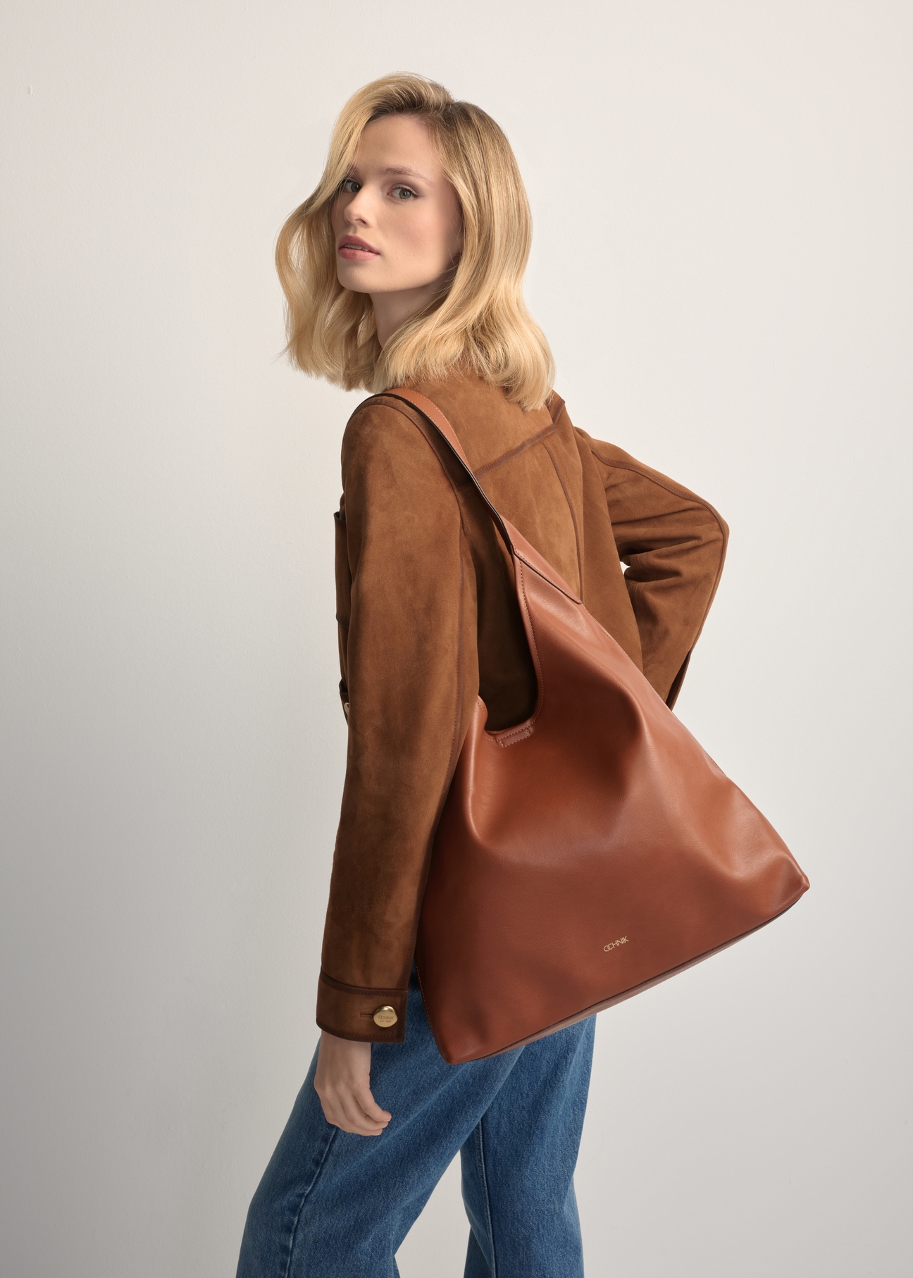 Duża torebka damska w kolorze koniaku TOREC-1199-1F(W26), widok produktu na ramieniu modelki. Widoczna połowa sylwetki.