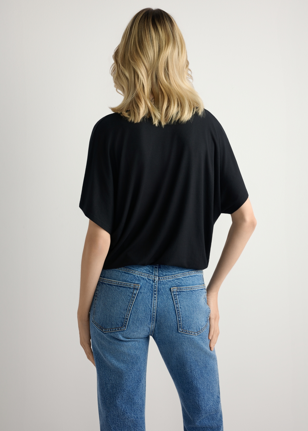 Czarna bluzka damska BLUDT-0202-99(W26), widok produktu z tyłu na modelce. Widoczna połowa sylwetki.